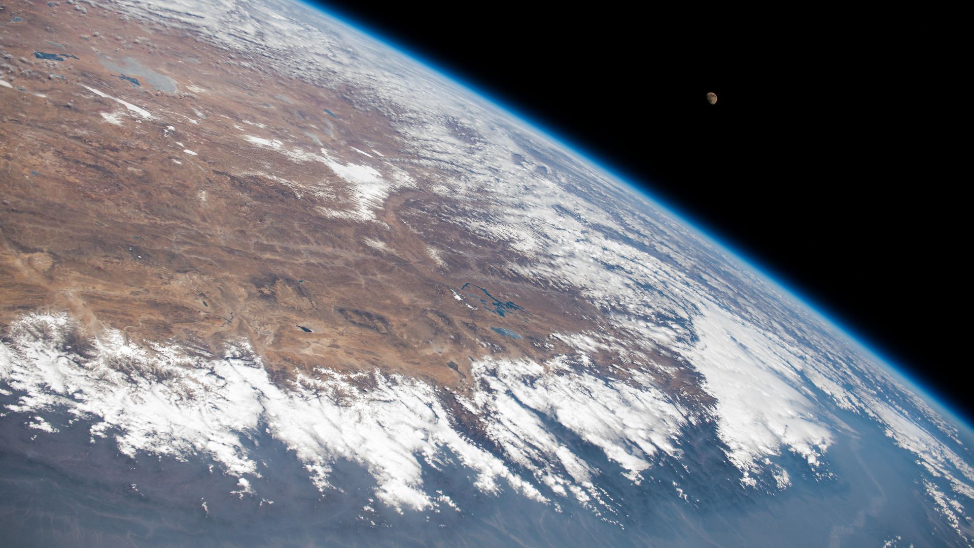 A half Moon rising above Earth, lit by the Sun.