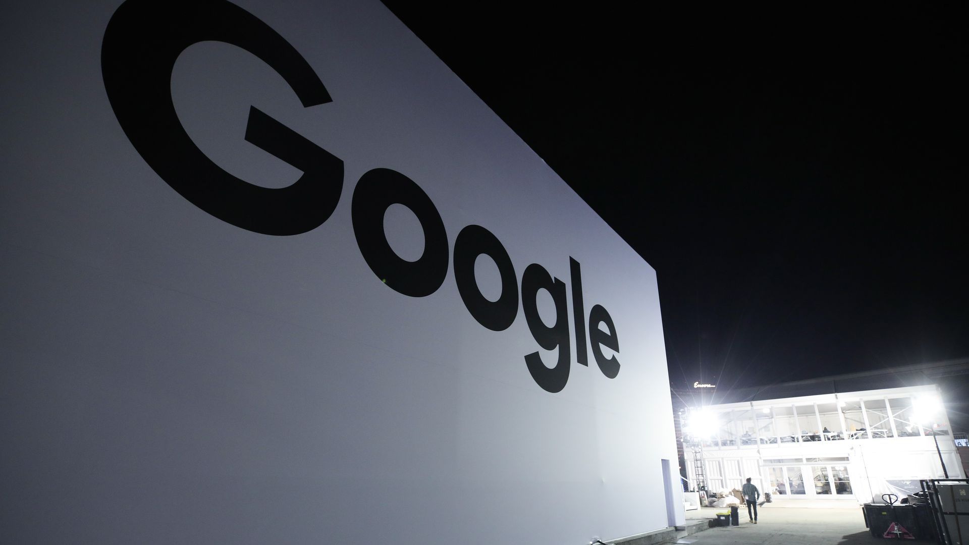 A Google sign at night, with lights in the background