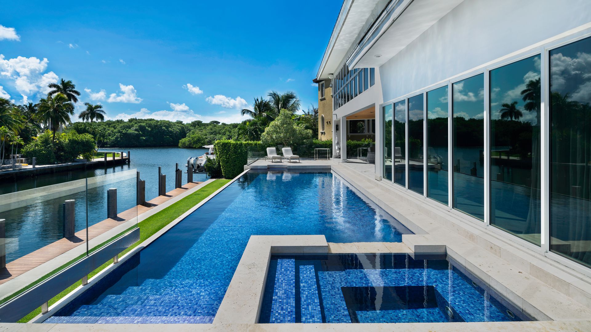 The back patio of a Coral Gables home shows a swimming pool looking at a canal.