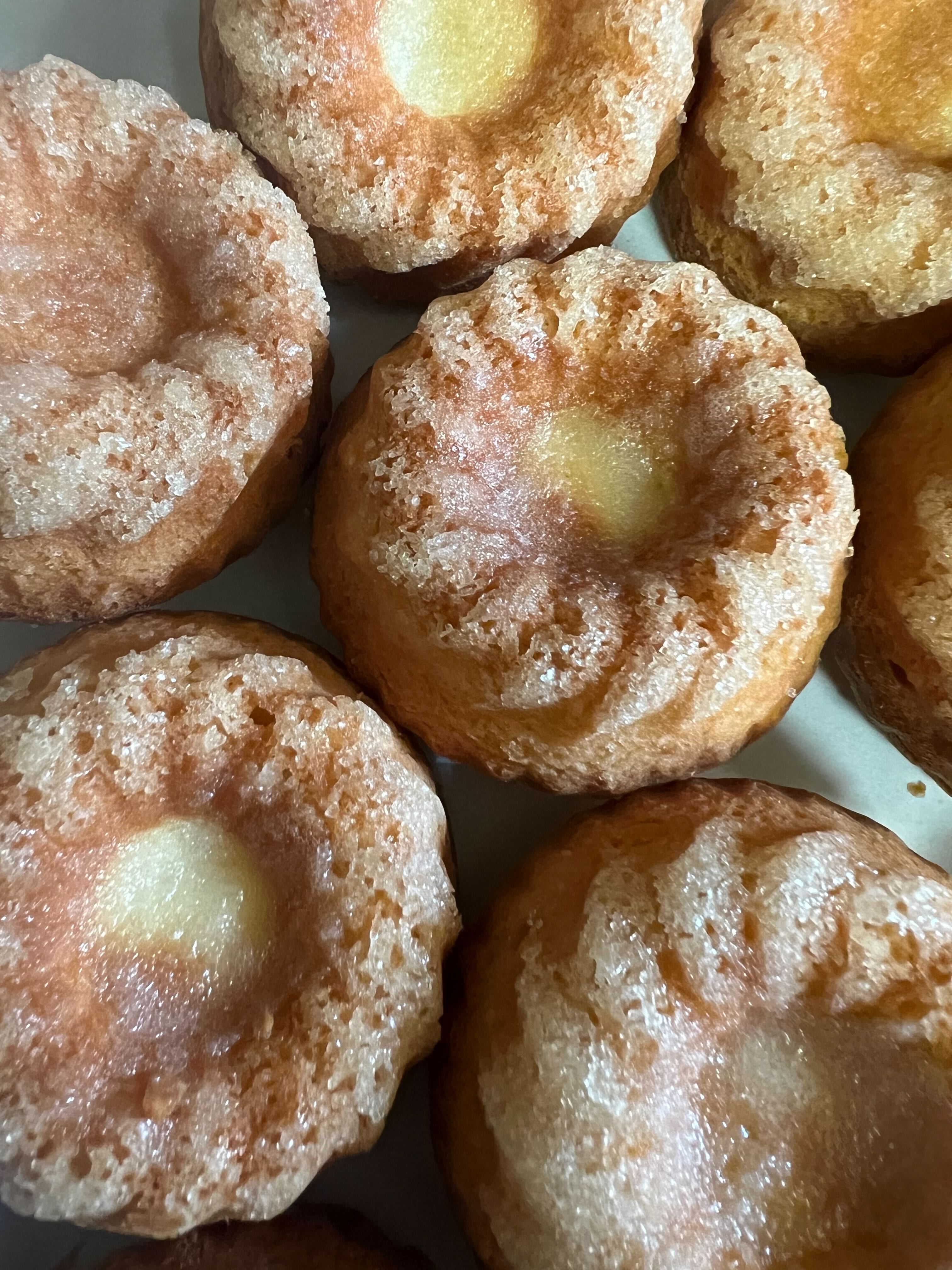 Close-up of golden brown, sugar-coated mini bundt cakes with a glazed center, arranged closely together on a white surface.
