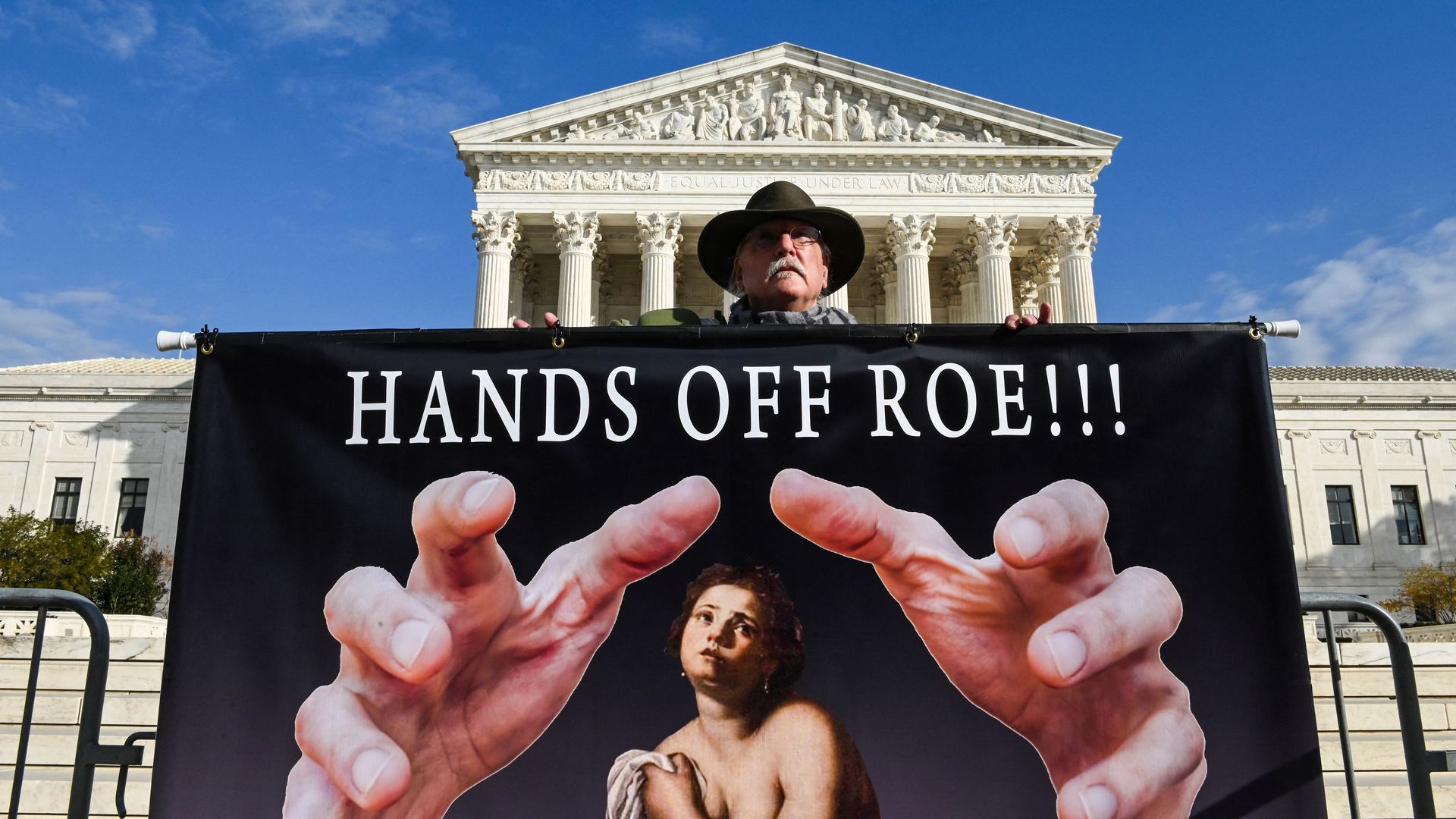 A man protesting a challenge to abortion rights is seen standing with a "Hands Off" sign outside the Supreme Court.
