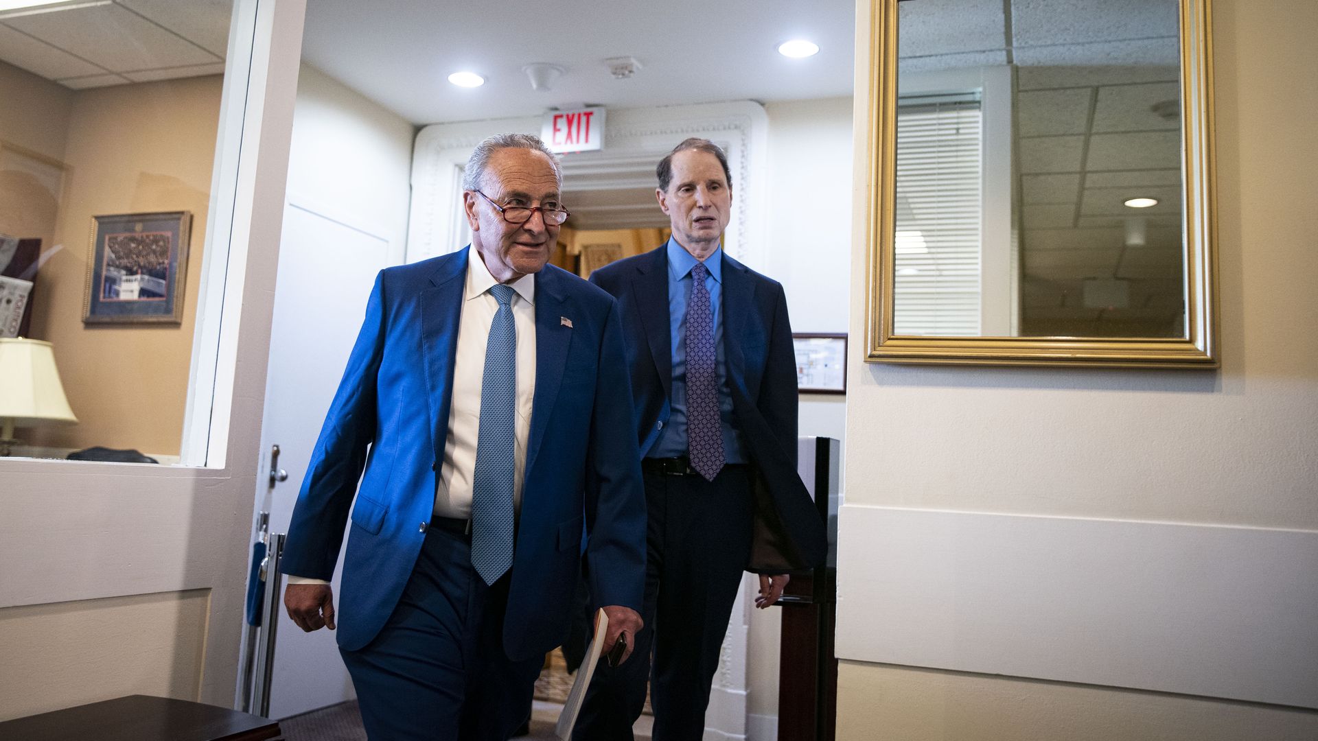Photo of Chuck Schumer and Ron Wyden in suits walking in the hall