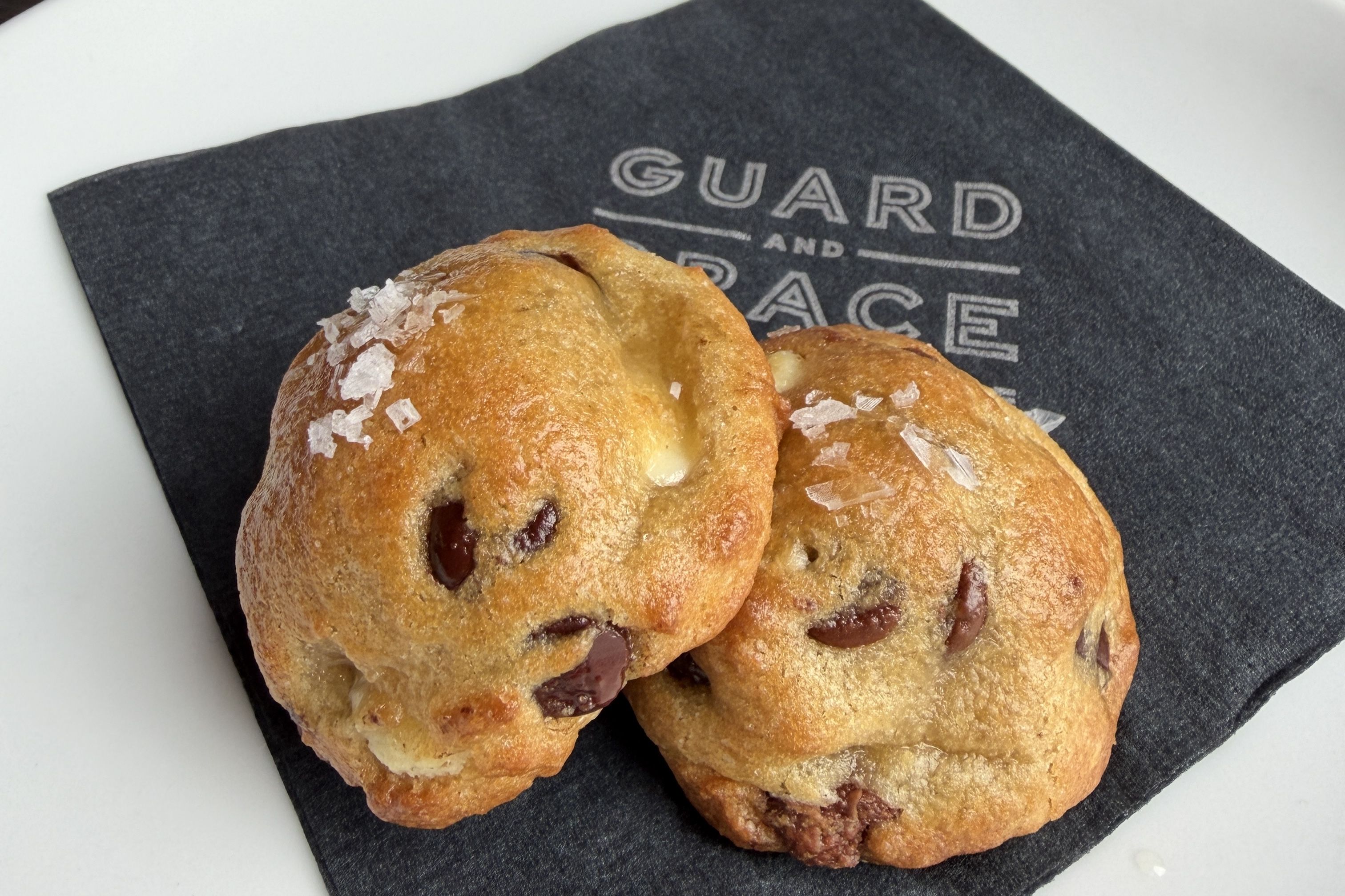 Three golden-brown pastries with visible red berry filling and flaky tops sprinkled with sugar, resting on a dark napkin with white lettering.