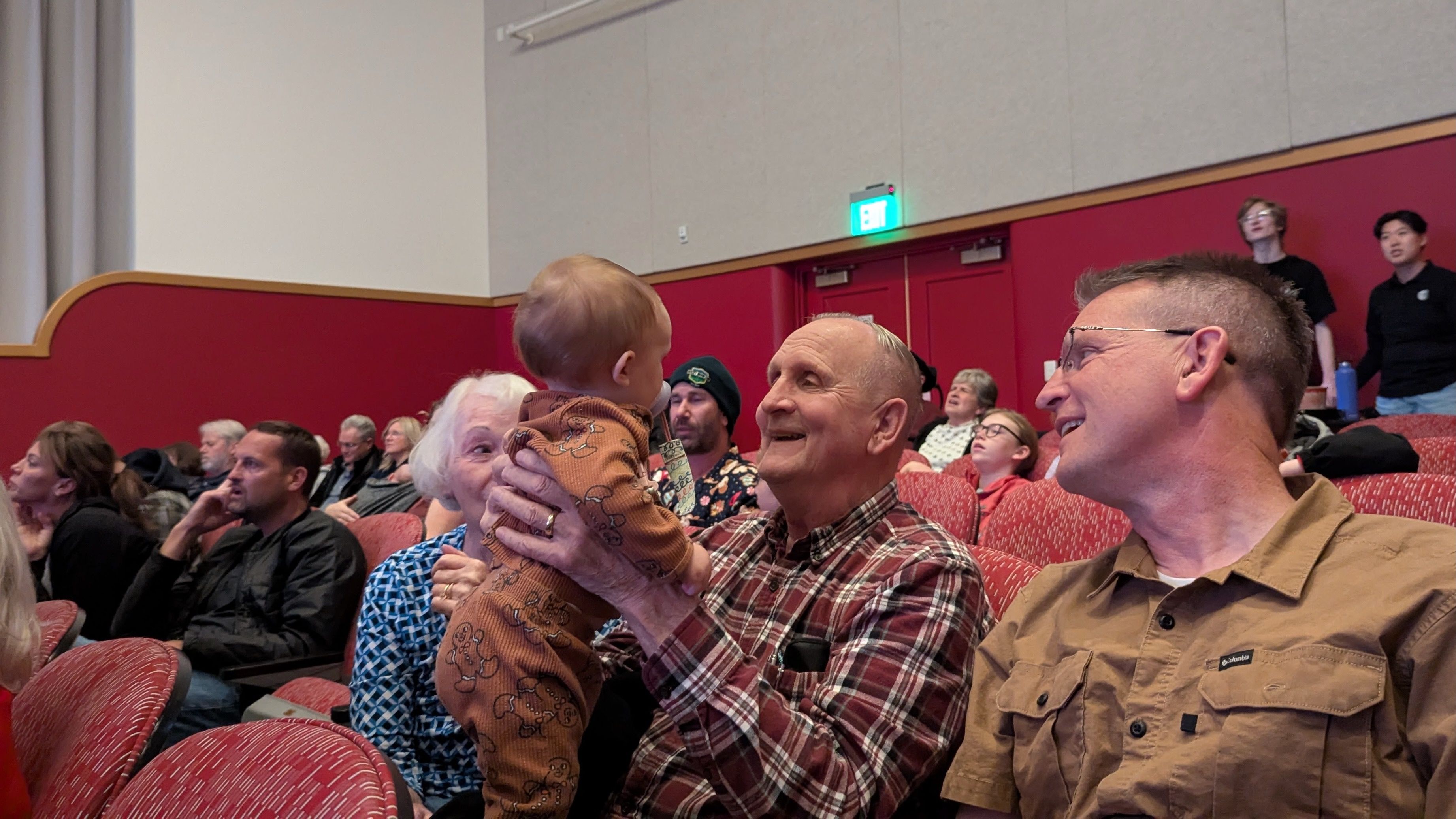 A man holds a baby while singing and smiling in a crowded theater 