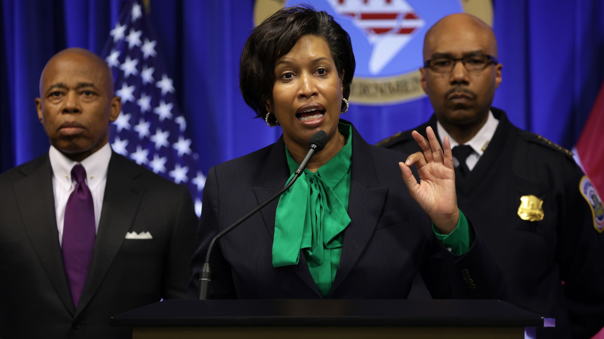 D.C. Mayor Muriel Bowser, center, is speaking at a podium with New York City Mayor Eric Adams on the left and D.C. police chief Robert Contee on the other side.