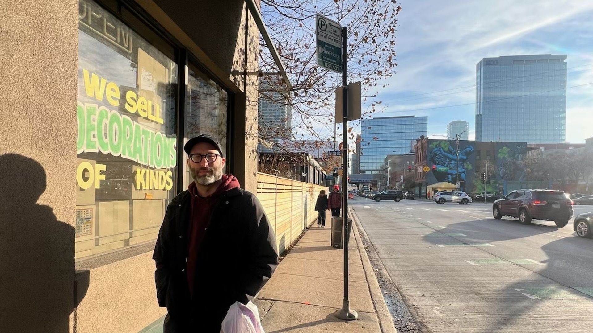 Photo of a man standing outside of a store as traffic drives by 