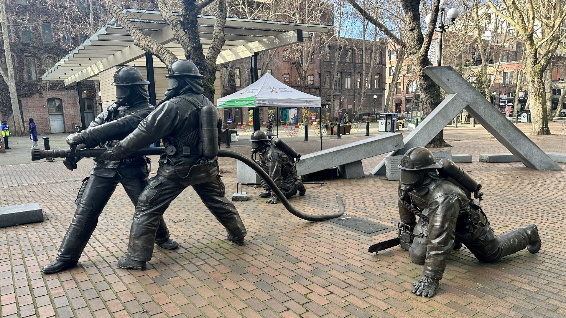 Four bronze statues in firefighter uniforms in different positions on a red brick square.