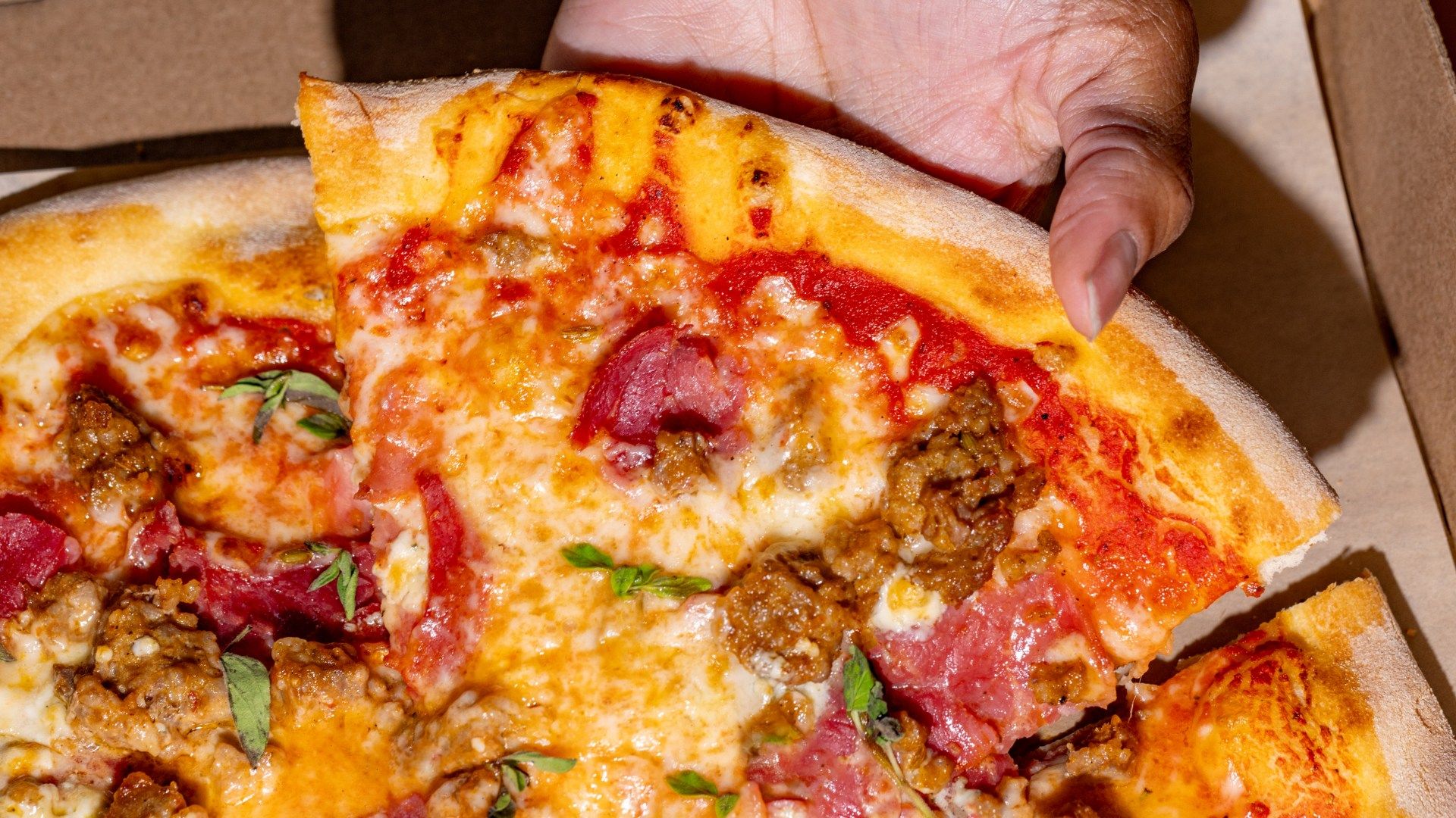  A close-up of a hand grabbing a slice of pizza. 