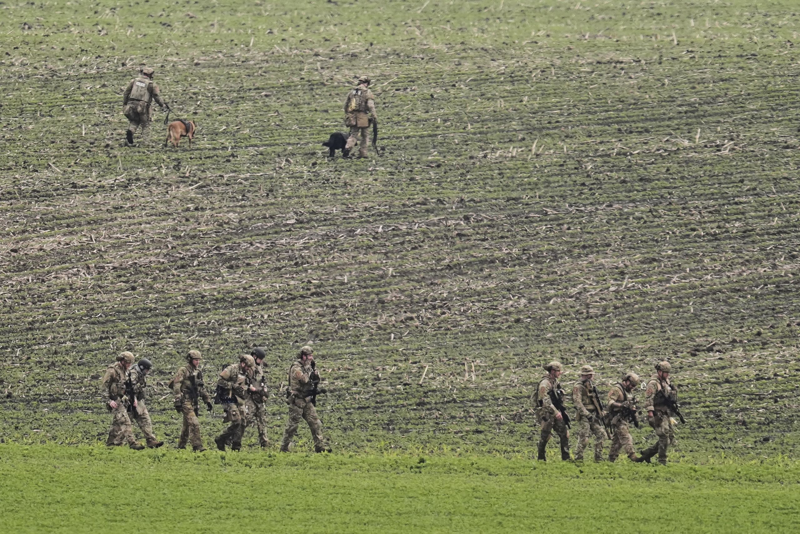 Law enforcement officers cross a field near a vehicle suspected to belong to shooting suspect Vance Boelter yesterday in Belle Plaine, Minn.