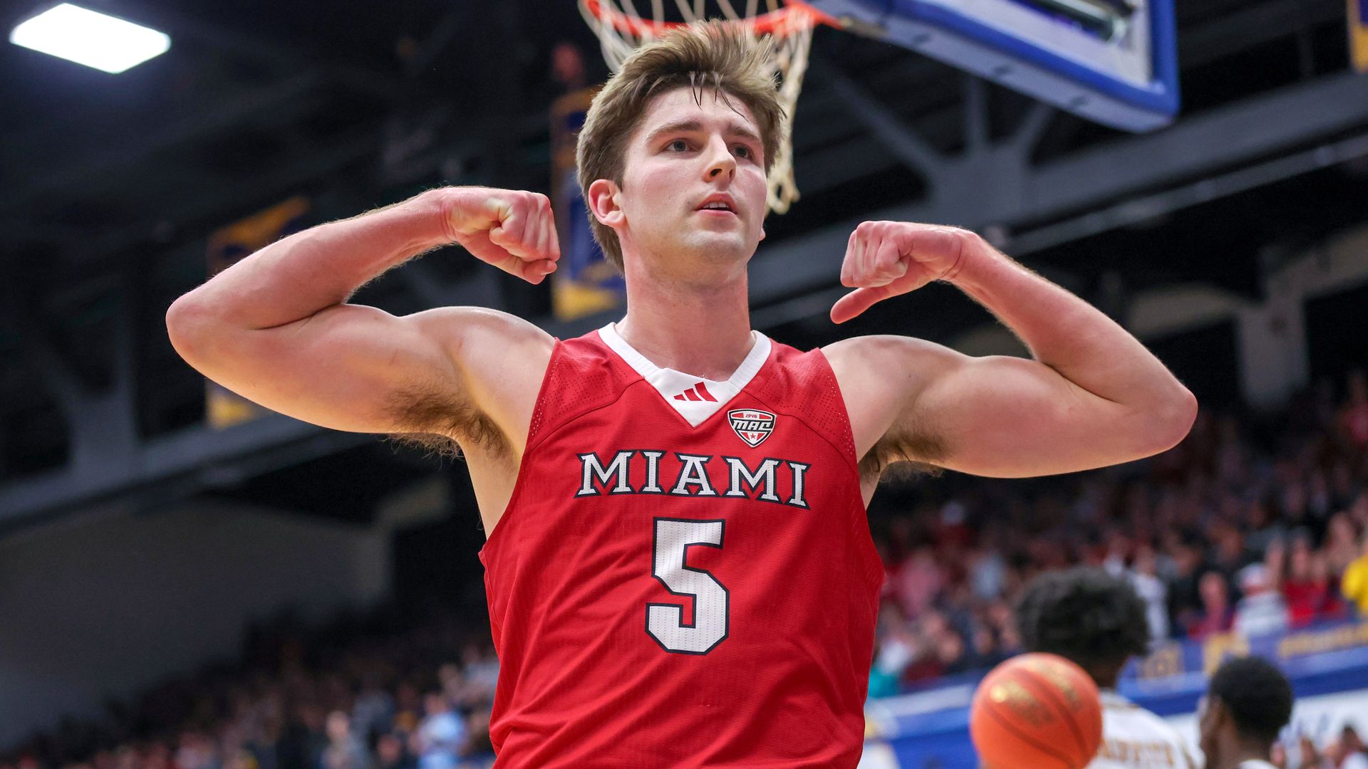White man in red "Miami" jersey (No. 5) flexes under a hoop. 