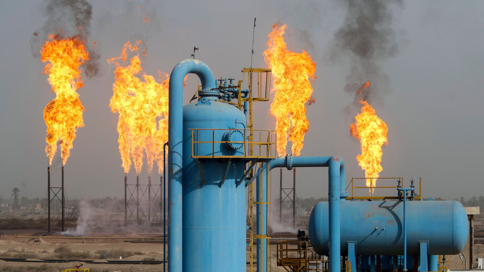 Flames in the background with smoke coming off them with teal-colored pipes in the foreground.