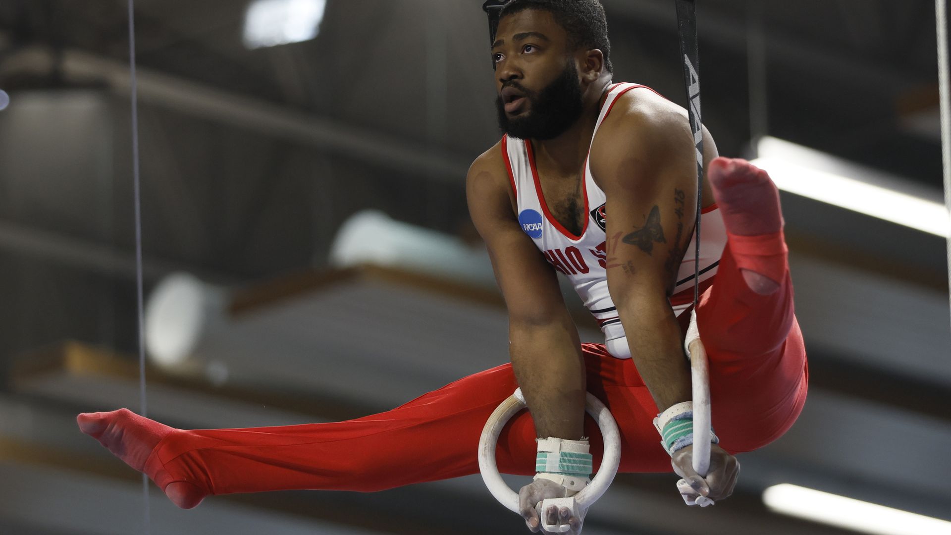 An Ohio State gymnast balances on the still rings with his legs in the air. 