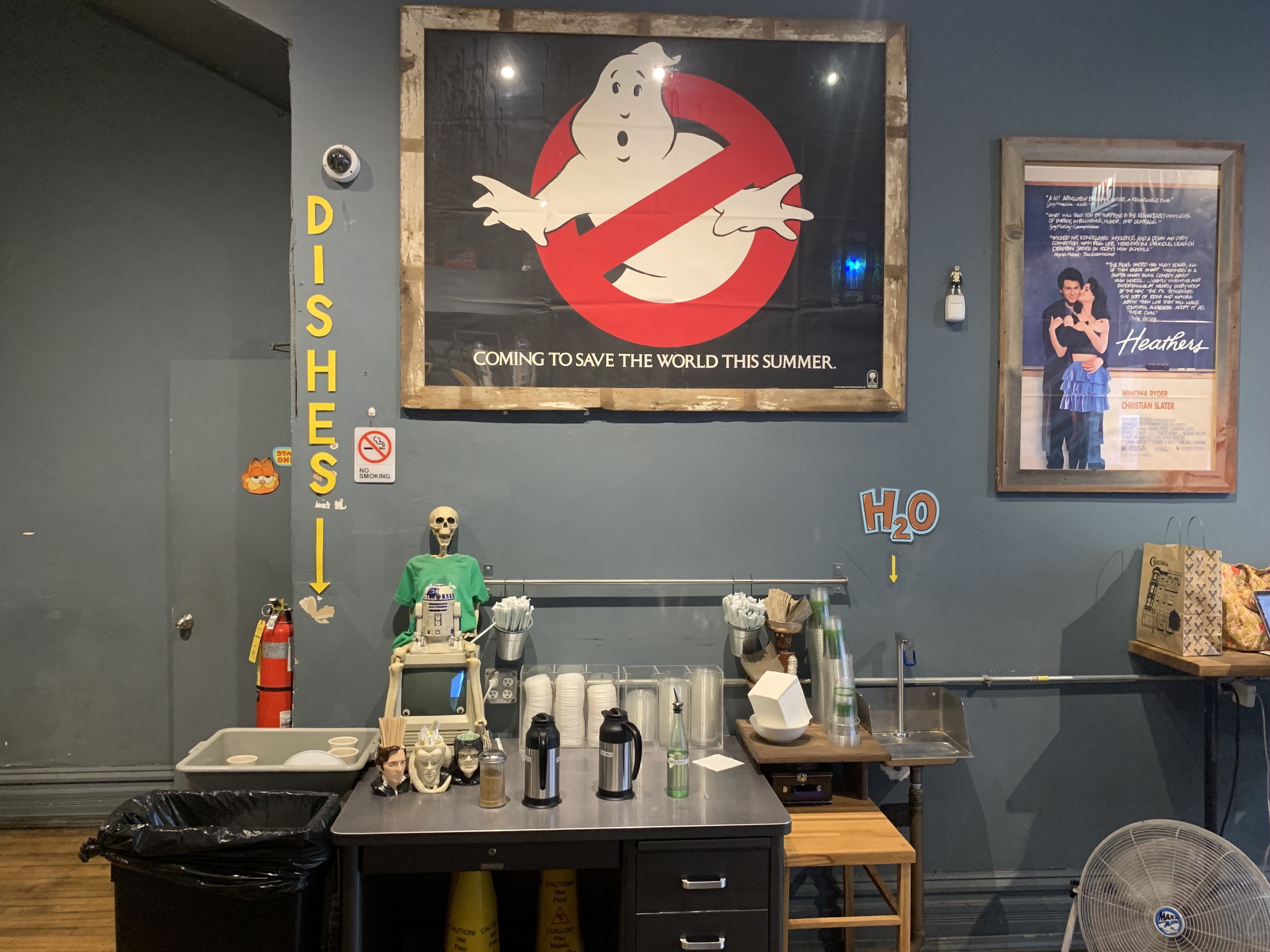 Photo of a movie poster hanging over a station with condiments, creams and napkins at a coffee shop.