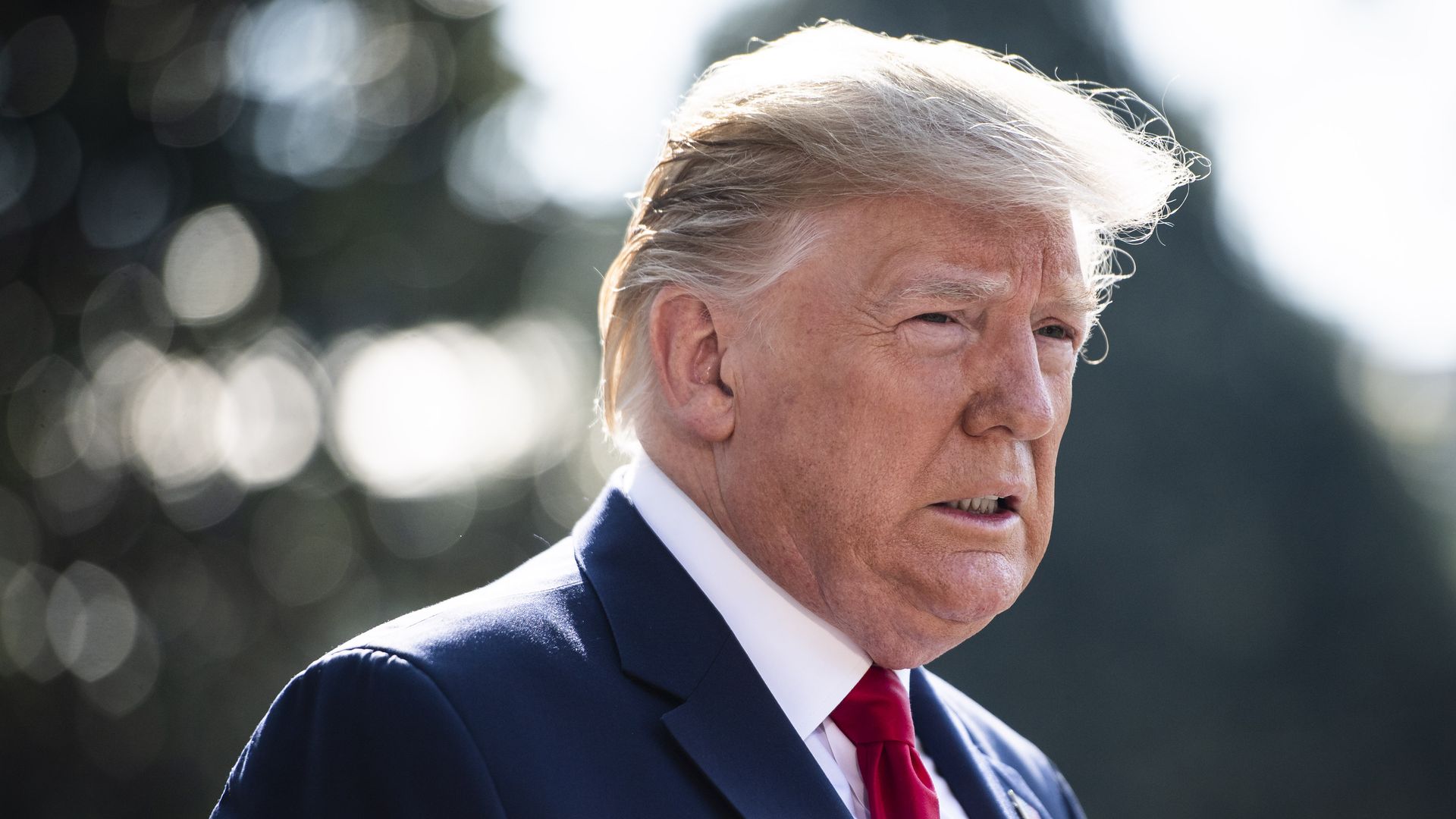 In this image, Trump stands outside in a suit and tie and faces reporters.
