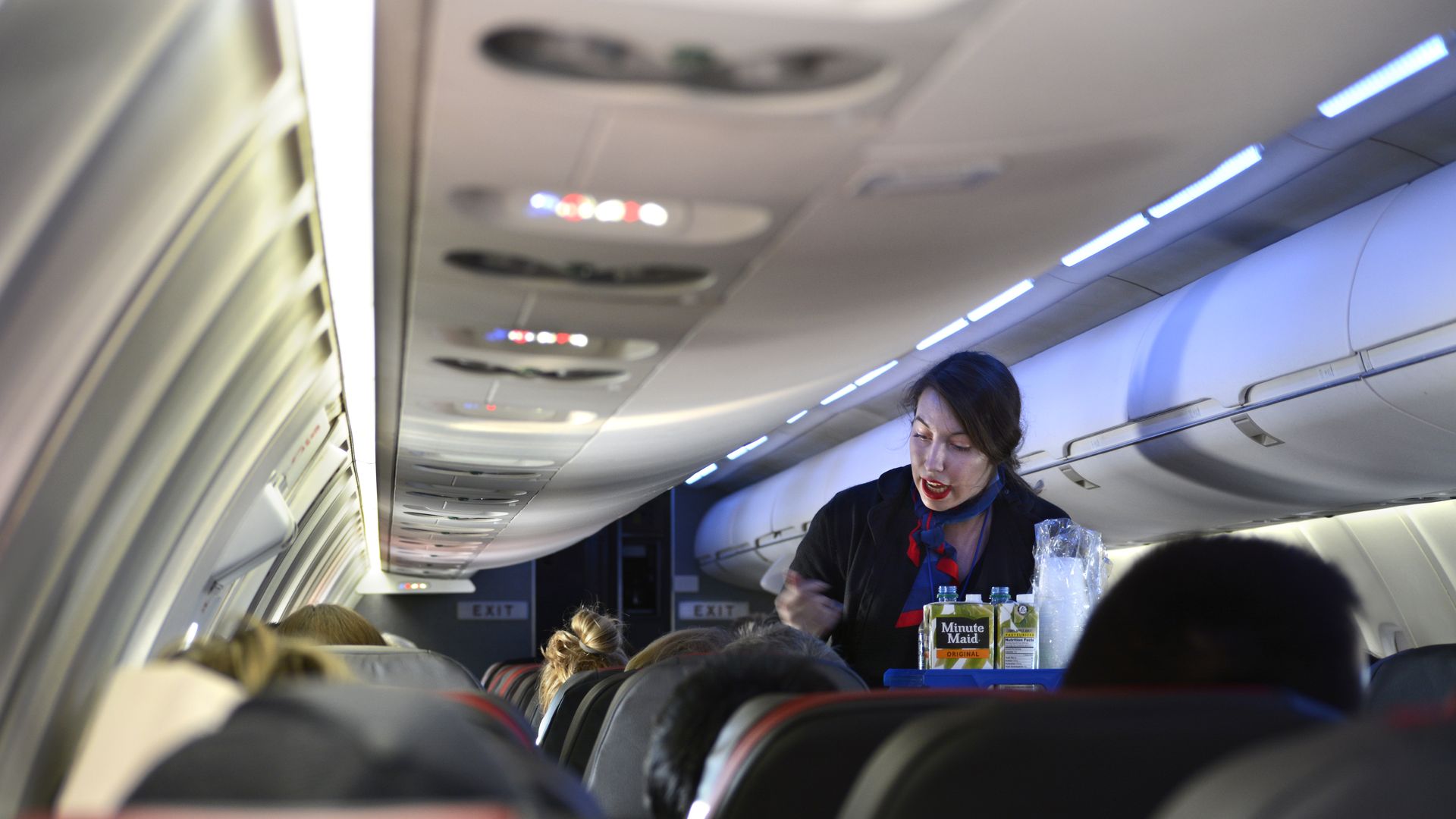 In this image, a stewardess walks down an airplane aisle offering drinks.