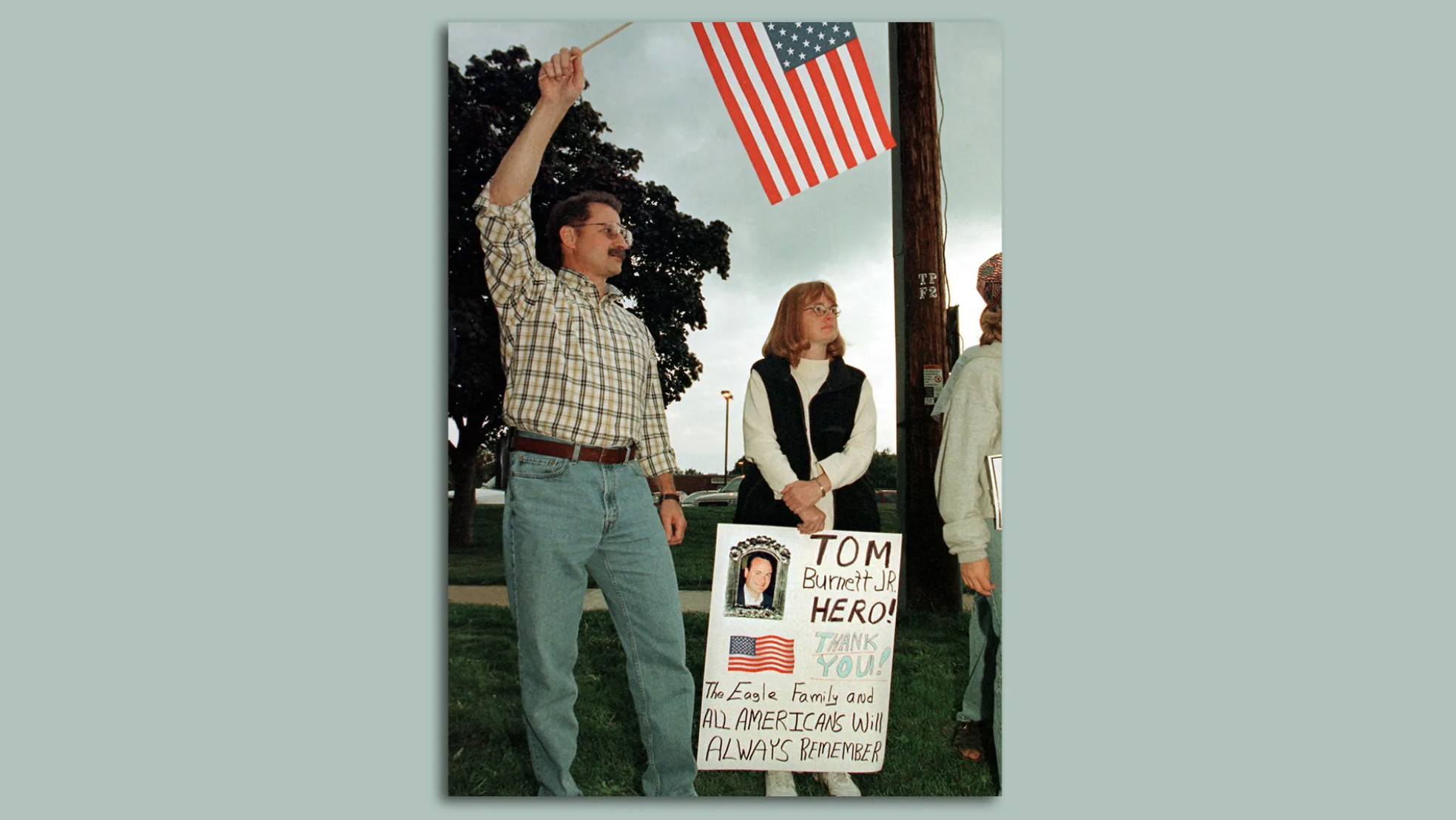A man and a woman with a flag and a sign honorin Tom Burnett.