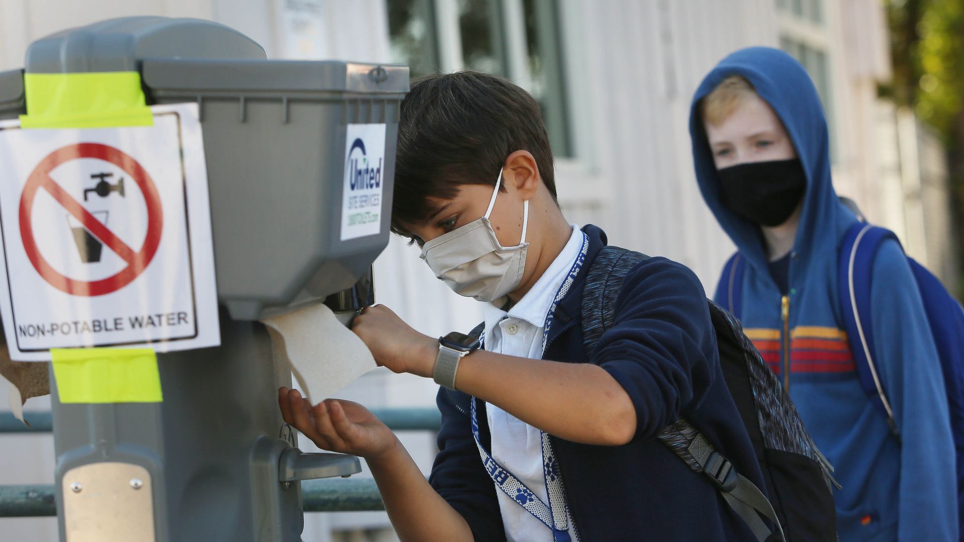 Kids use hand sanitizer while wearing face masks.