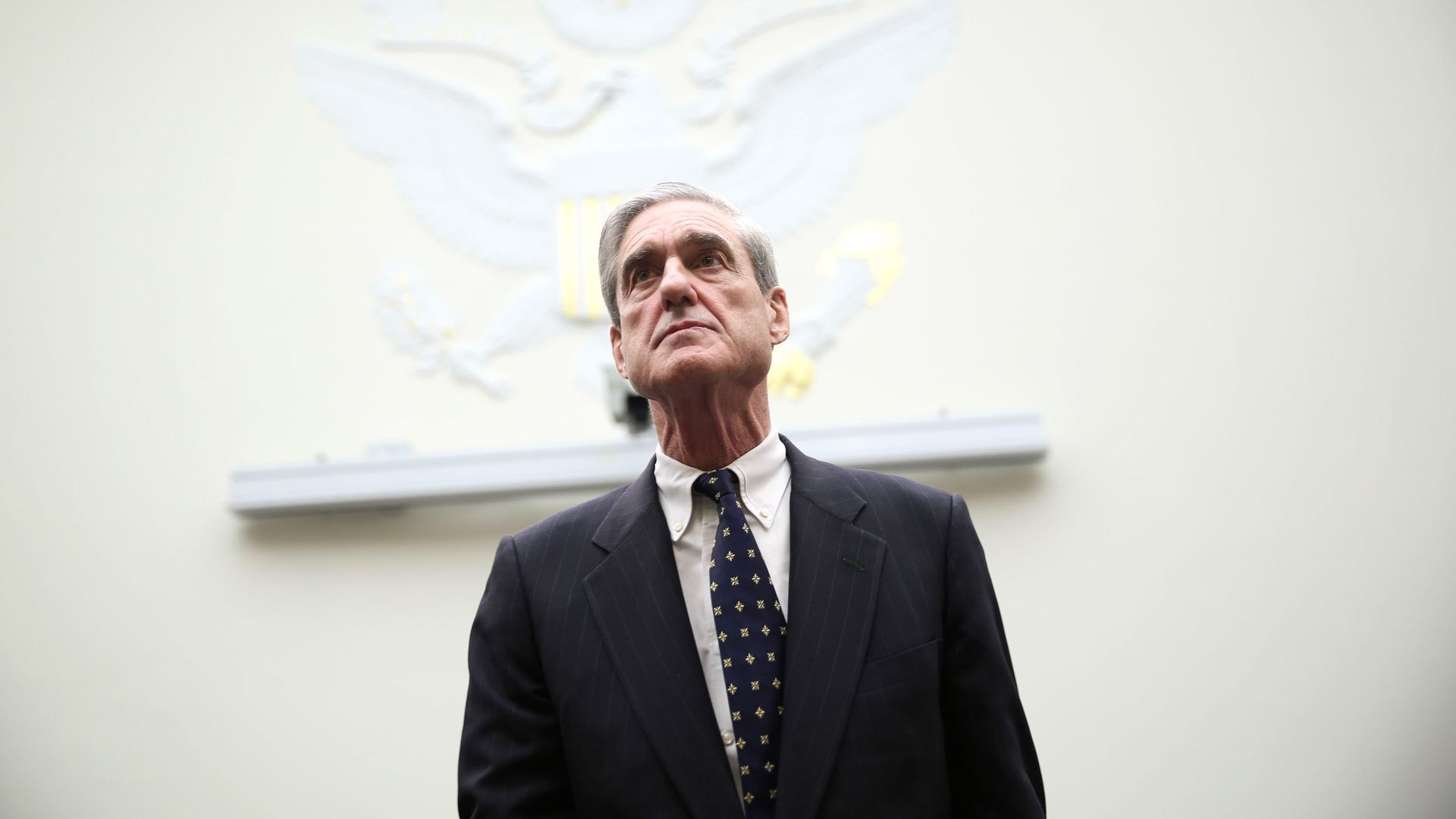 In this image, special counsel Robert Mueller stands in front of a white background. 