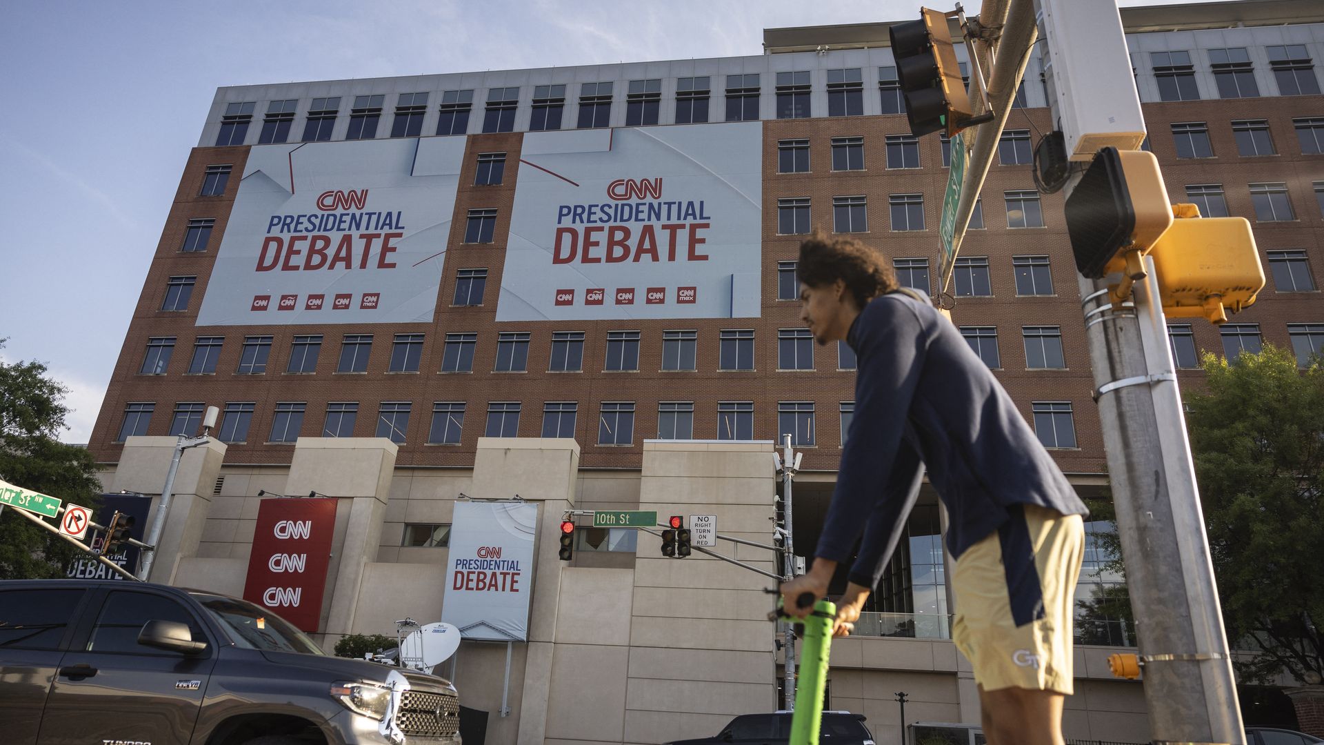A person rides a scooter outside of a mid-rise office building with banners reading "CNN PRESIDENTIAL DEBATE"