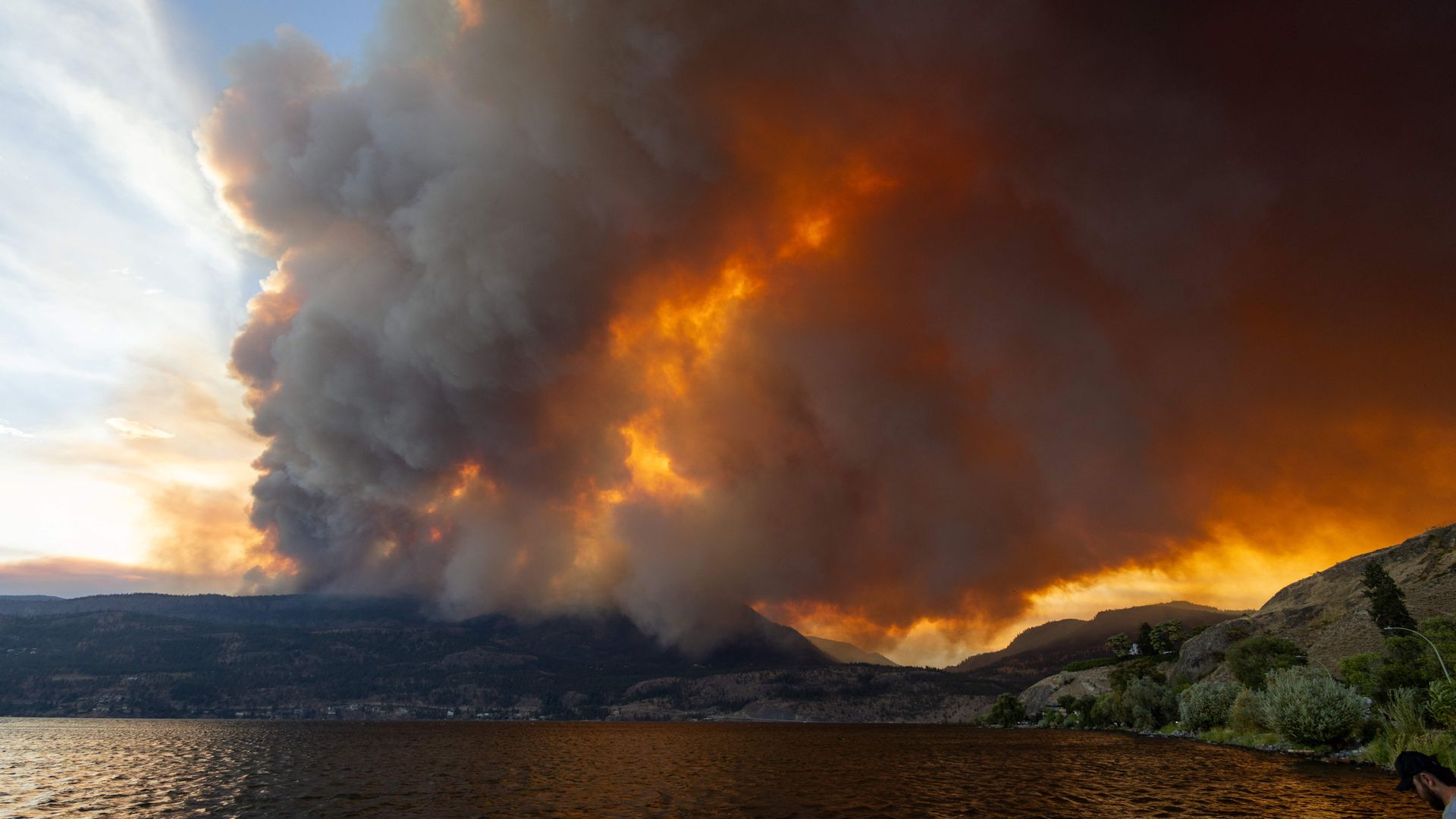Photo of a plume of dark smoke seen from across a lake as a wildfire burns.