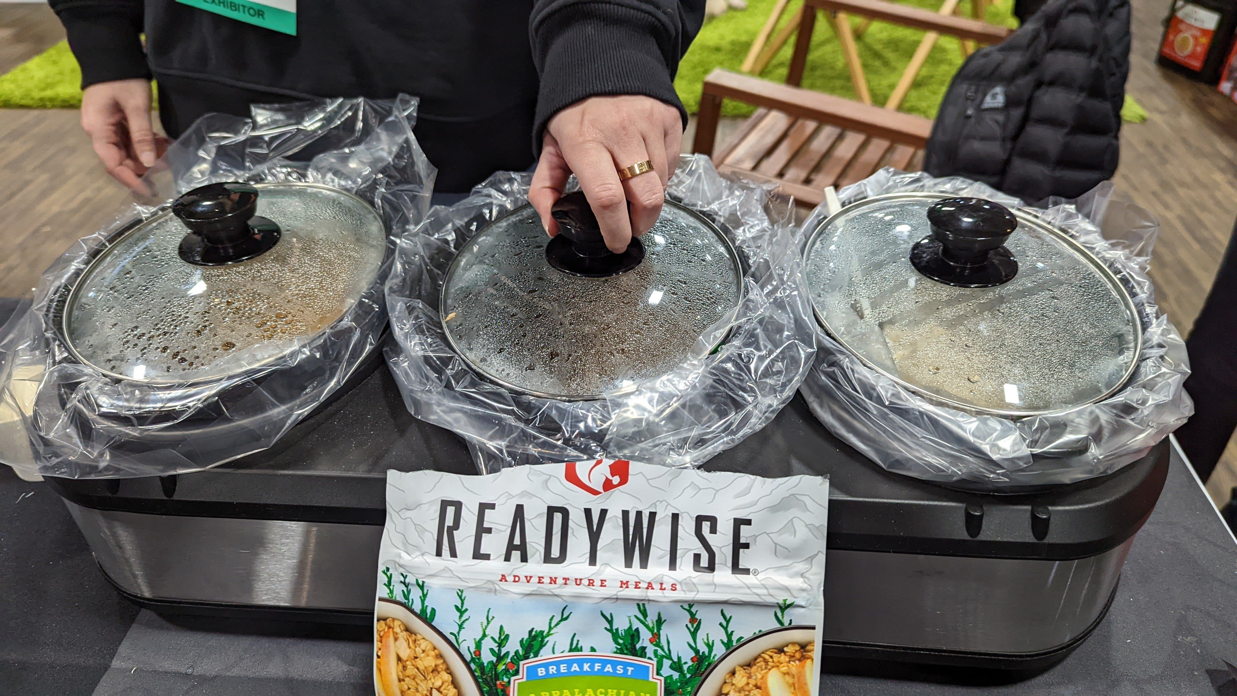 Food is in warming dishes next to a "ReadyWise" backpacker meal package.