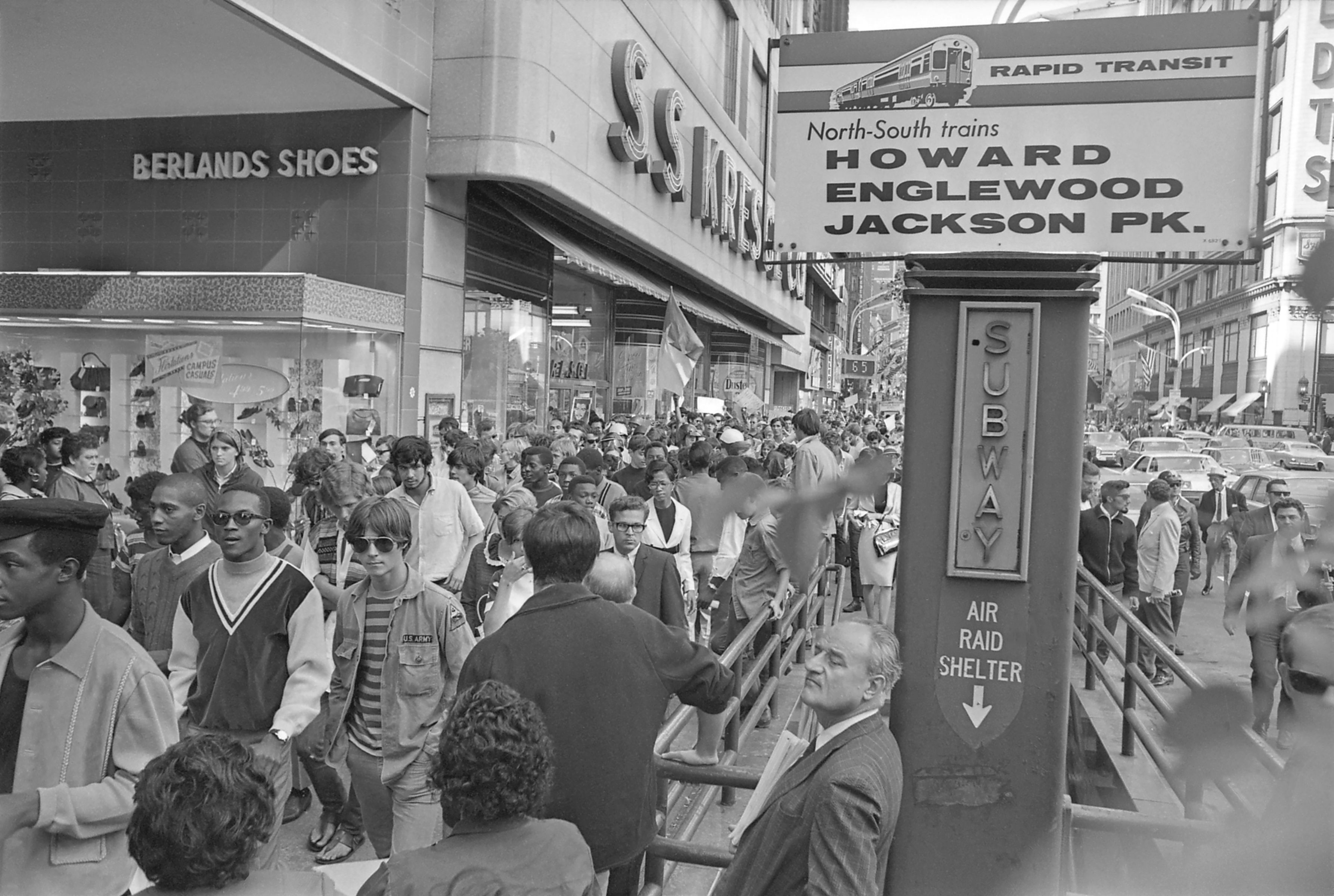 Photo of people crowding along a street in front of a store 