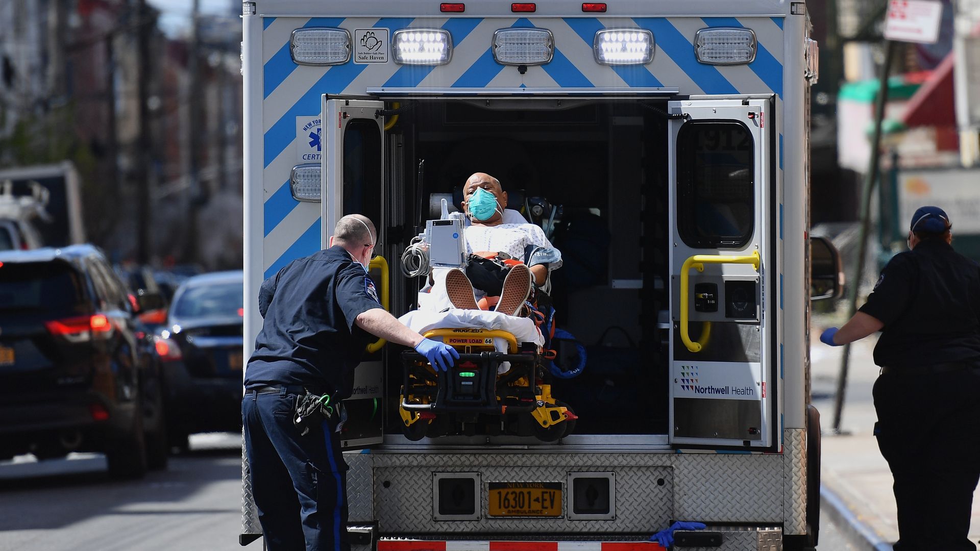 A photo of paramedics loading a man wearing a face mask into an ambulance.
