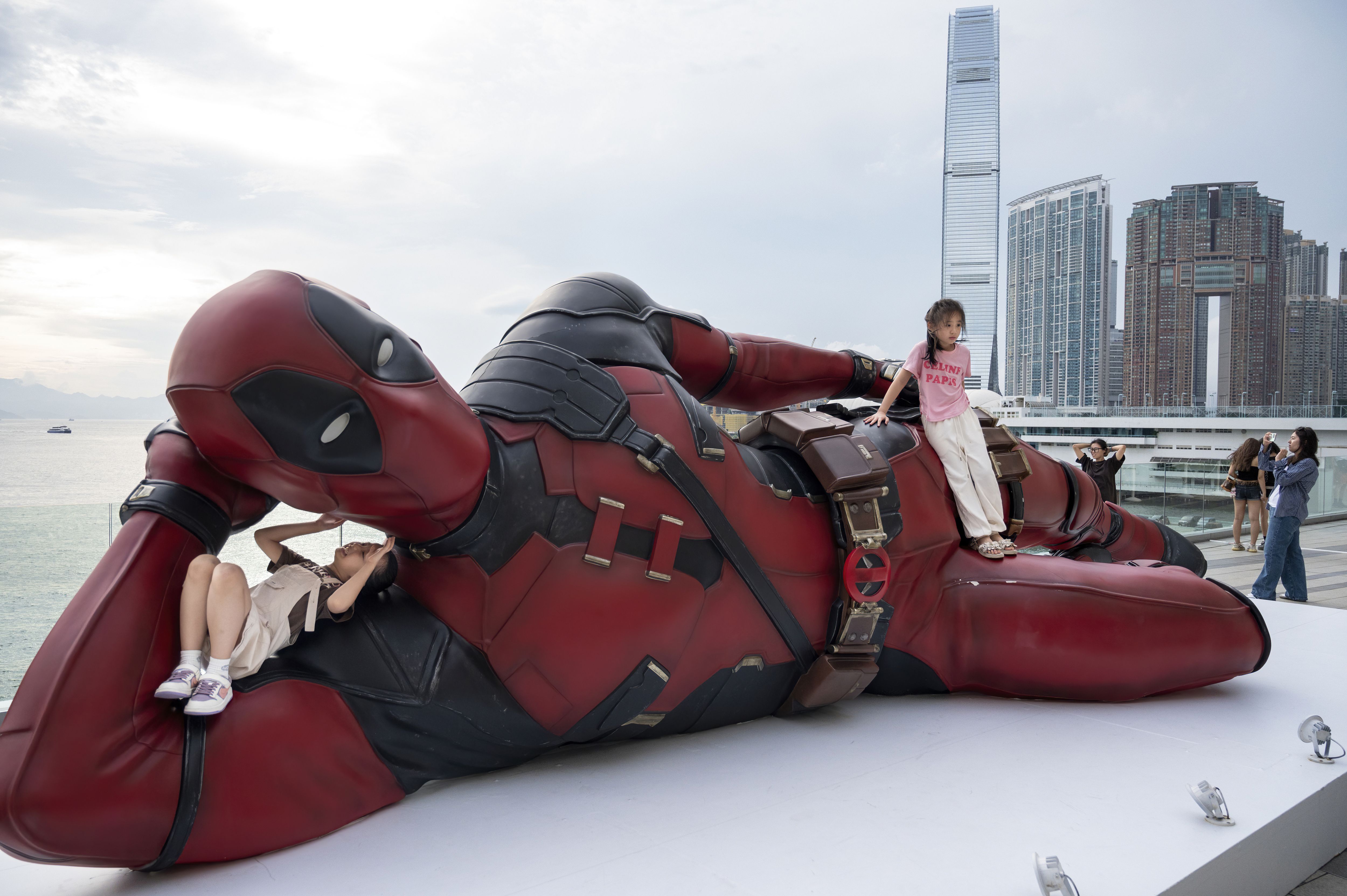 HONG KONG, CHINA - 2024/08/18: Children climb an 8-meter installation of Marvel's Deadpool character as tourists and locals take photos with the set up to promote the new movie 'Deadpool & Wolverine' released under Disney in Hong Kong. (Photo by Miguel Candela/SOPA Images/LightRocket via Getty Image