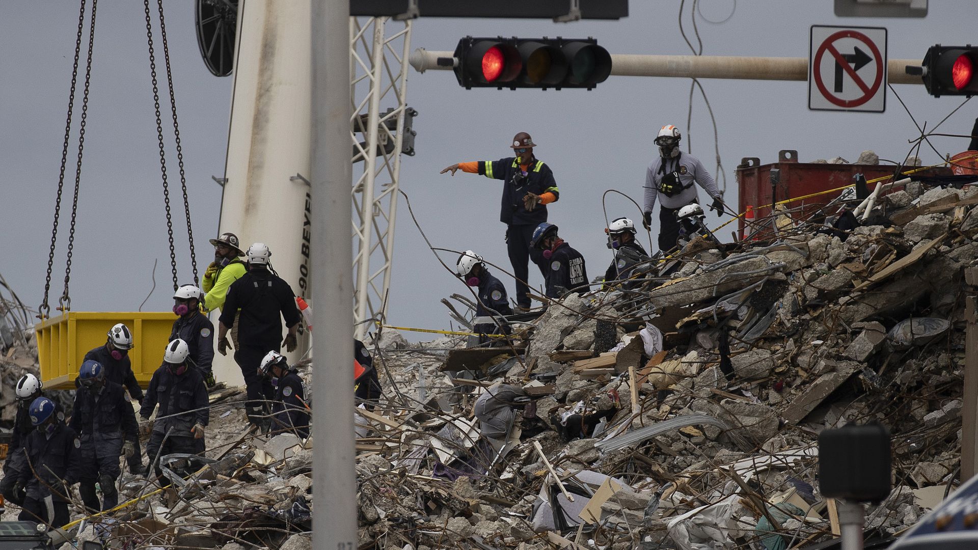 Photo of search and rescue workers climbing over rubble, with collapsed traffic lights hanging over them