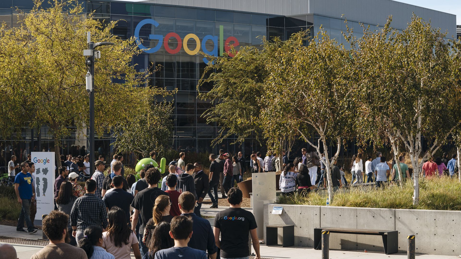 In this image, a large crowd of people walk towards a Google office during a walkout protest