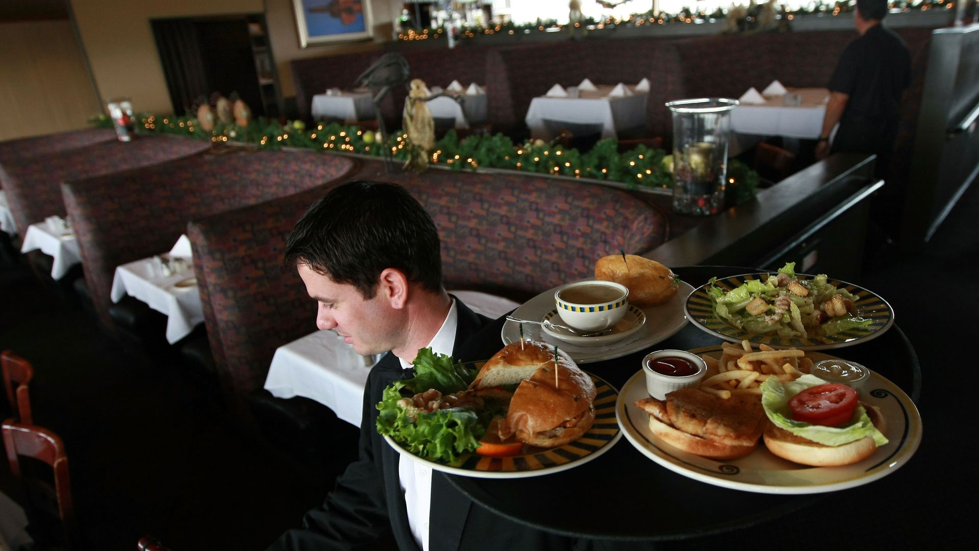 In this image, a waiter carries several entree plates while walking through a restaurant.