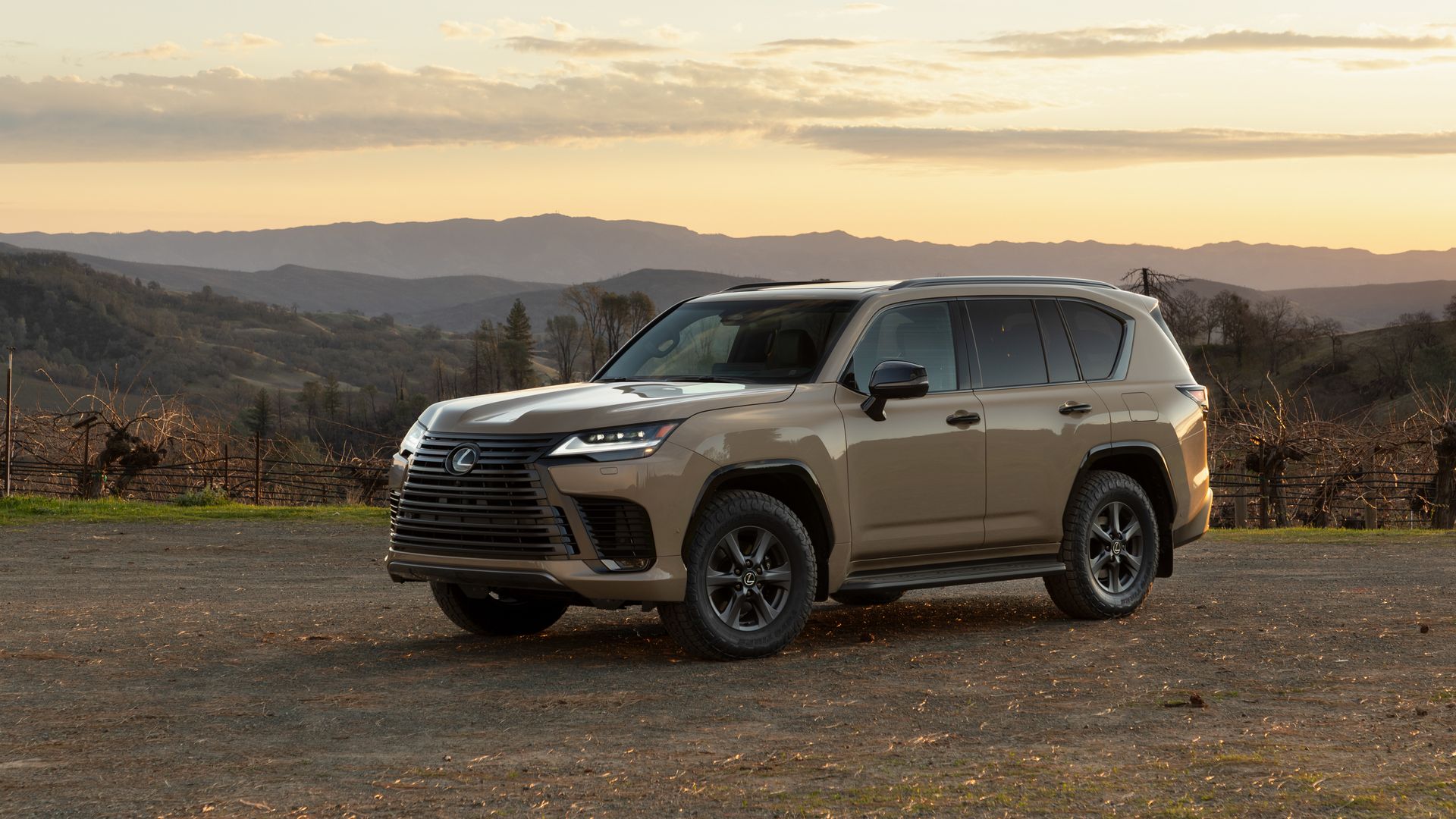 Image of a beige "earth"-colored Lexus LX700h SUV, parked among mountains at sunset