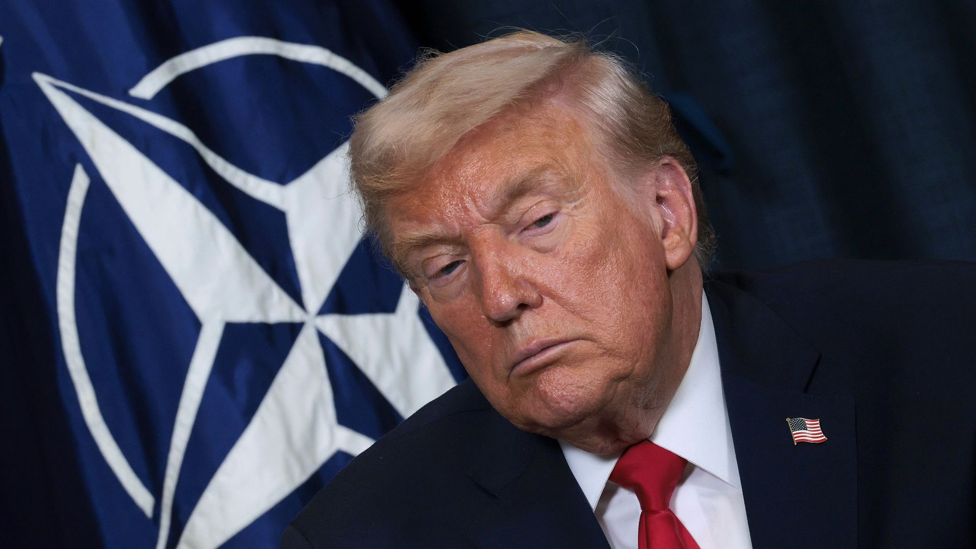 Trump wearing a navy suit jacket, white collared shirt and red tie while looking down with a straight expression