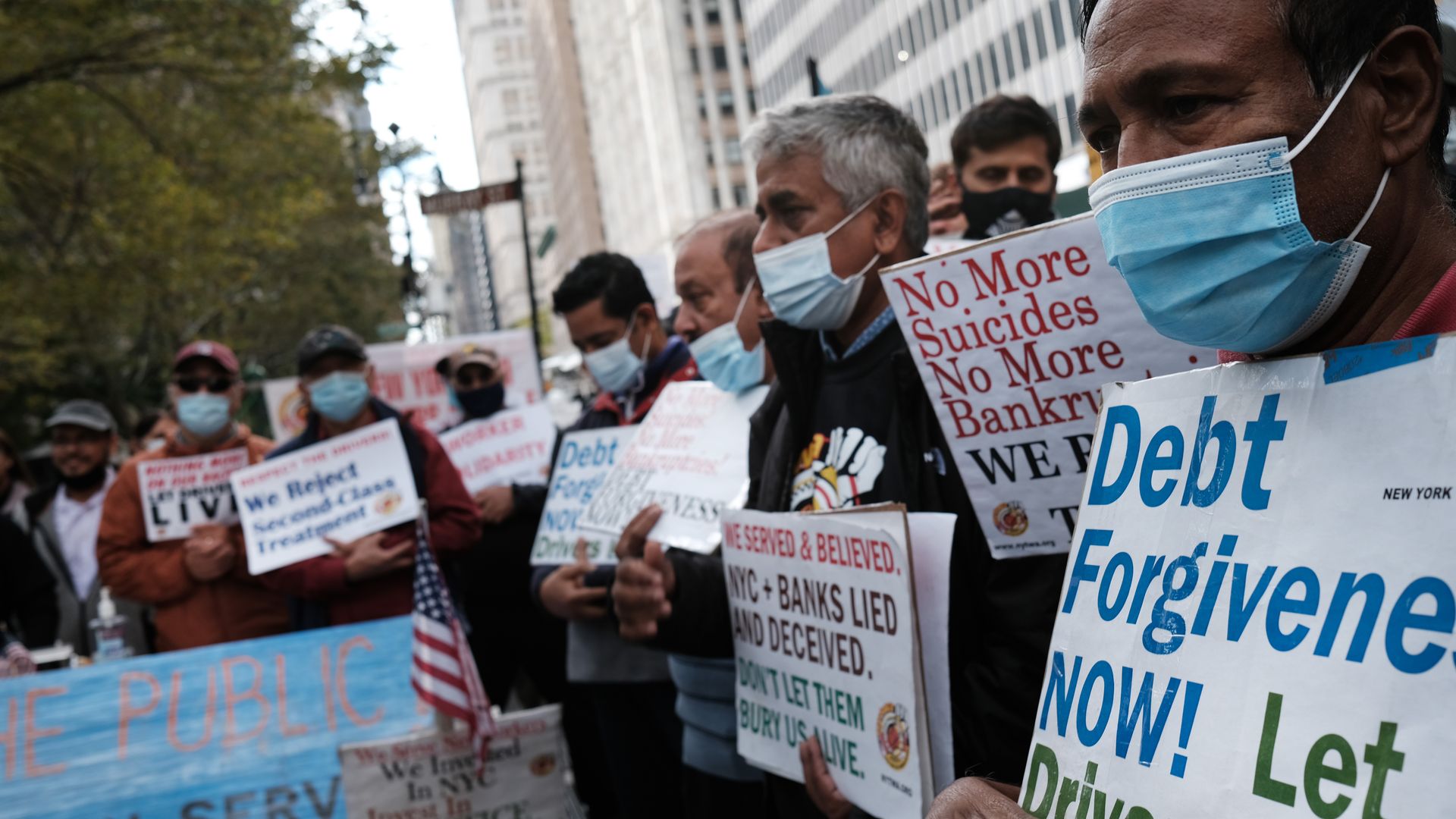 Photo of crowded protesters holding up signs that say "Debt forgive now!" and "No more suicides!" in an outdoor rally