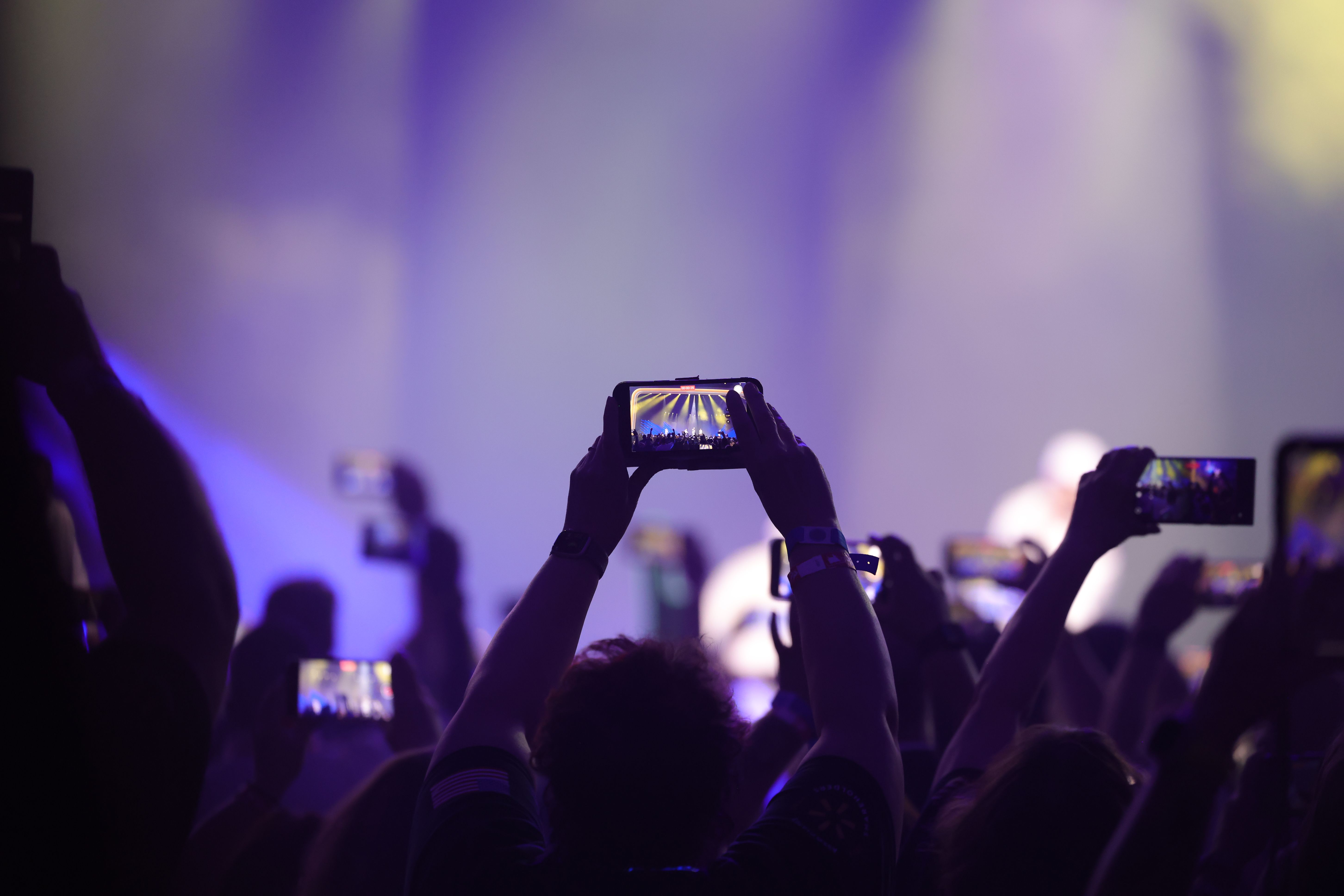 Members of a crowd video a show on a stage with their phones. 
