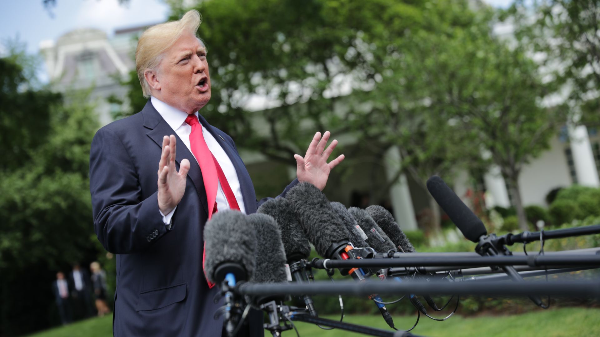 President Donald Trump's hair blows in the wind while he speaks to reporters and gestures with his hands