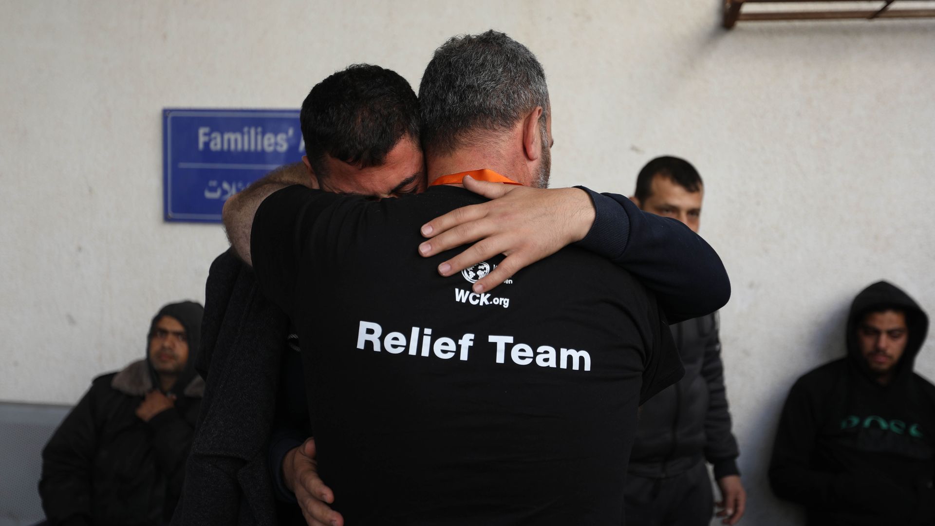 Two men, one wearing a black World Central Kitchen "relief team" t-shirt, hug each other as they receive the bodies of aid workers who were killed by Israeli air strikes in Gaza.