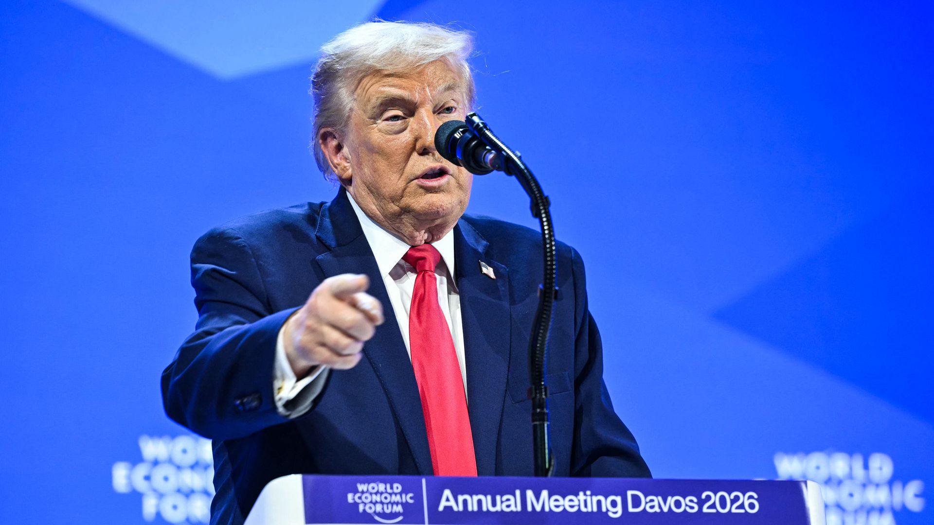 Trump, wearing a blue suit, white shirt and red tie, speaks into a microphone against a blue backdrop that reads "World Economic Forum." 