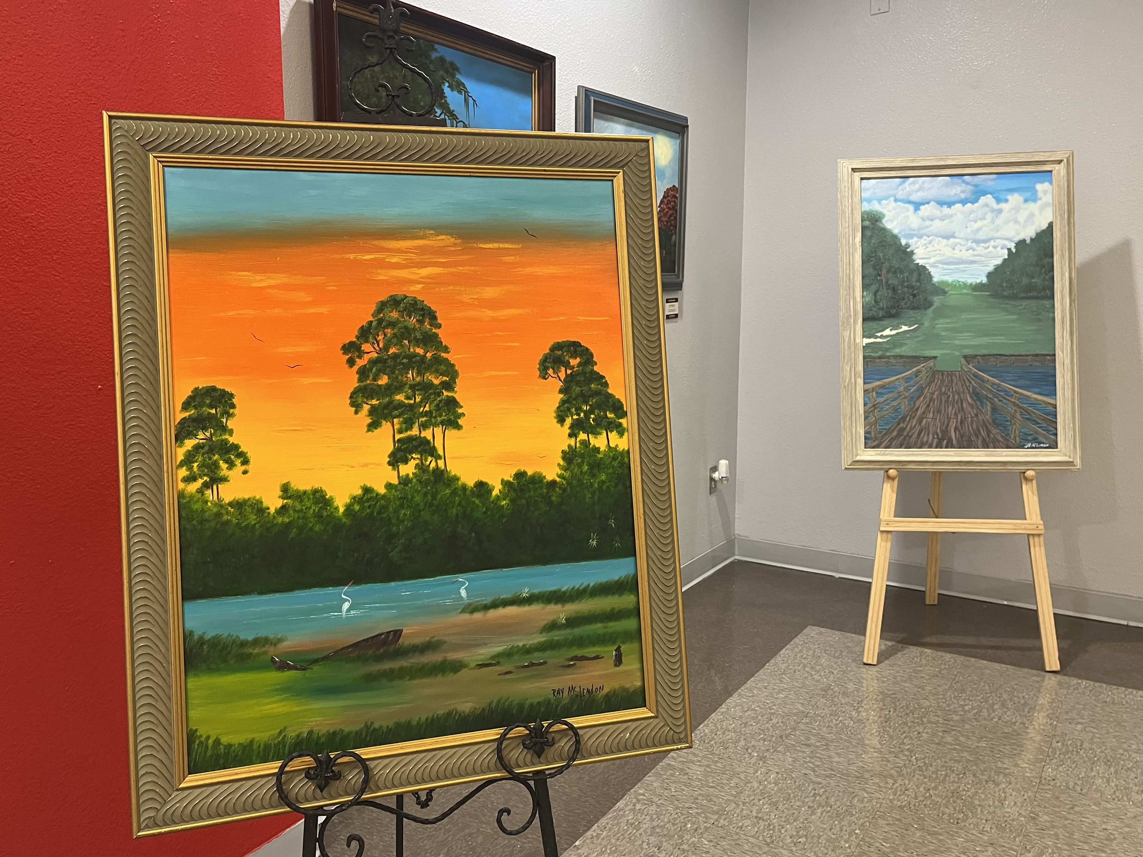 Two paintings, one of an orange-yellow sunset over a lagoon, the other of a bridge looking onto green water.