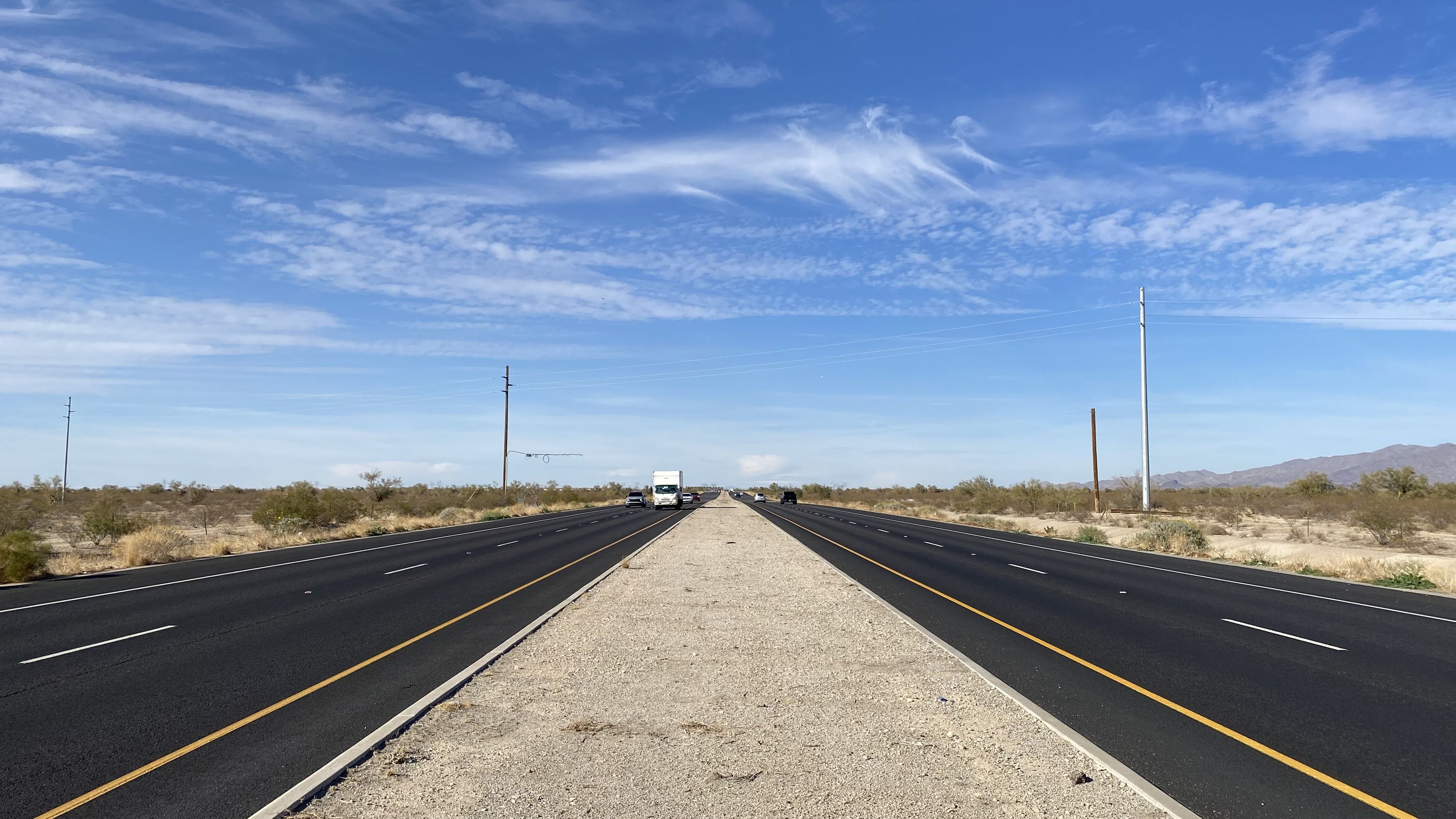 A four-land highway with a dirt median extends to the horizon through vacant desert land. 