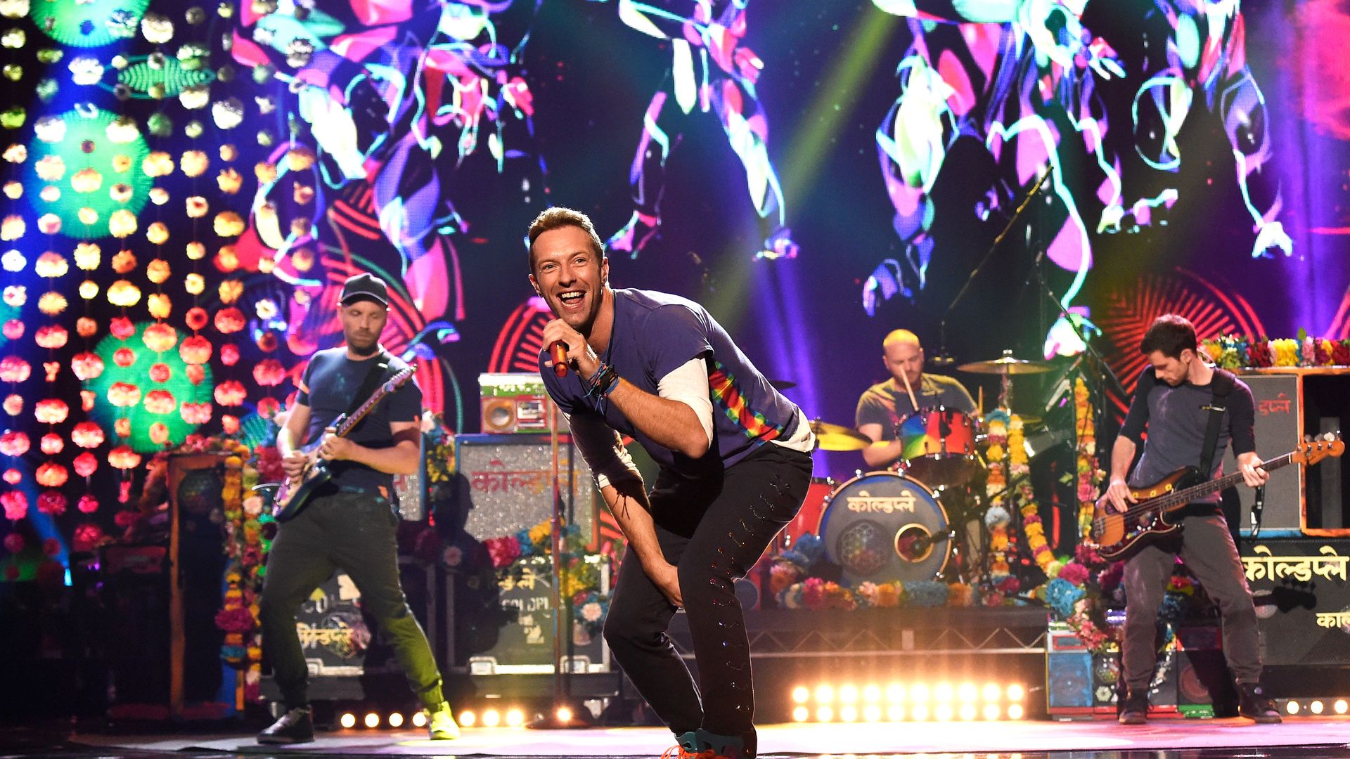 The members of the band Coldplay perform on stage in front of a bright LED screen.