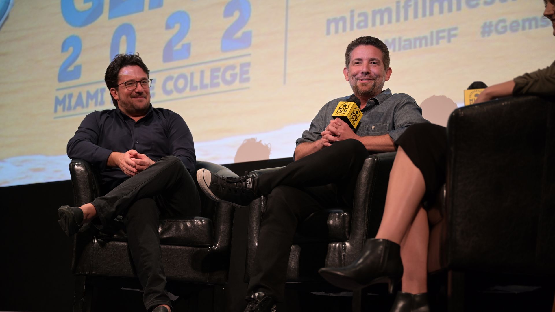 Two men sit on a stage holding microphones.