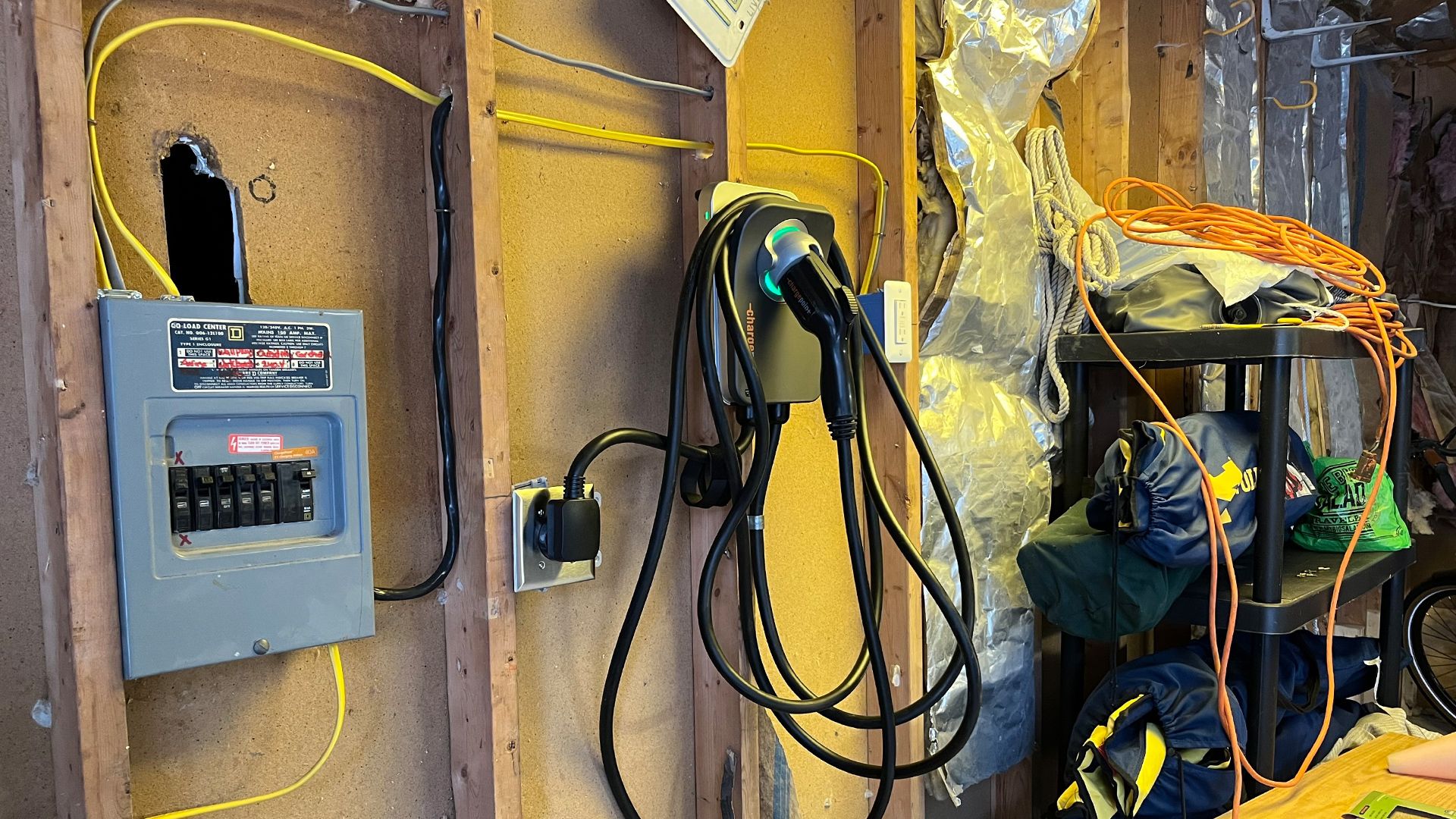 Image inside the author's garage, with an electrical panel in the foreground, and an electric vehicle charger mounted on the wall. 