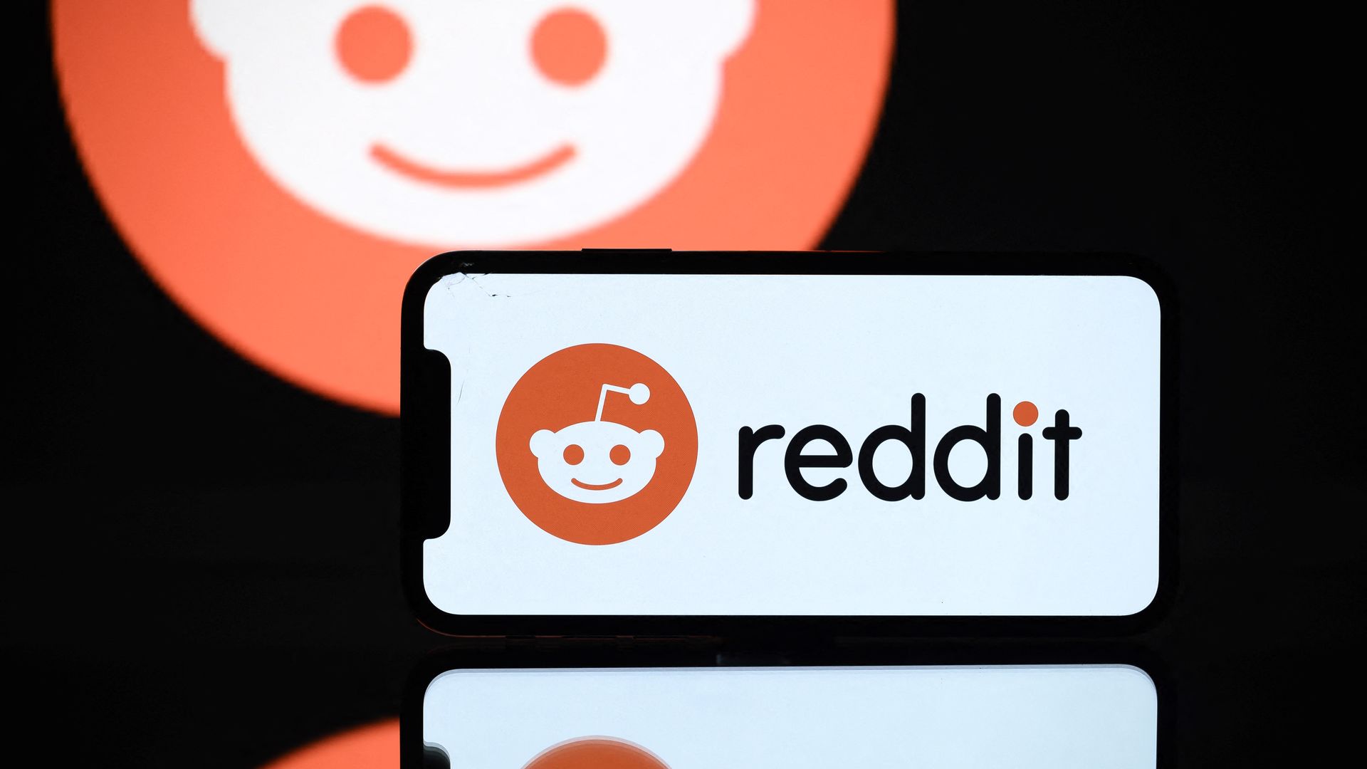 The reddit logo on and behind a phone