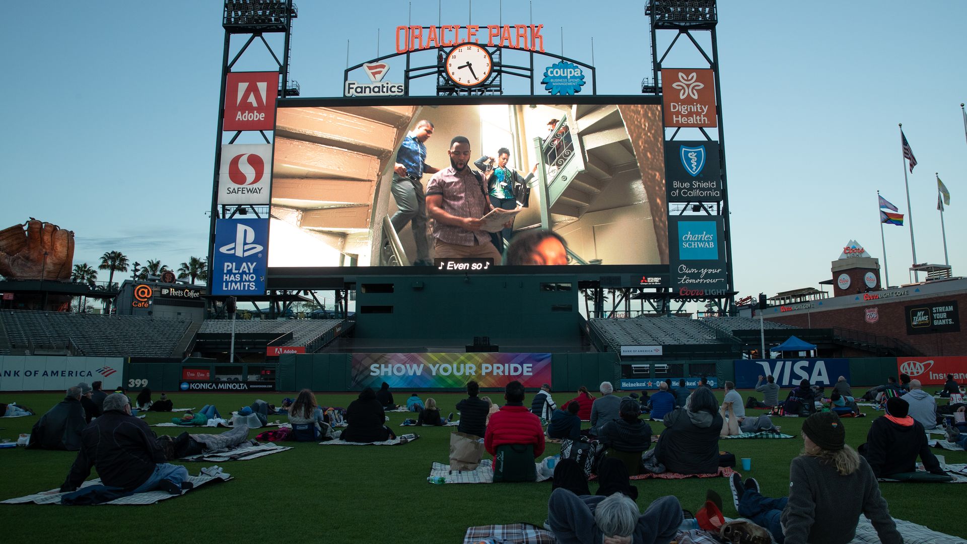 Photo of people lounging on the field at Oracle Park while watching "In the Heights" on a large screen