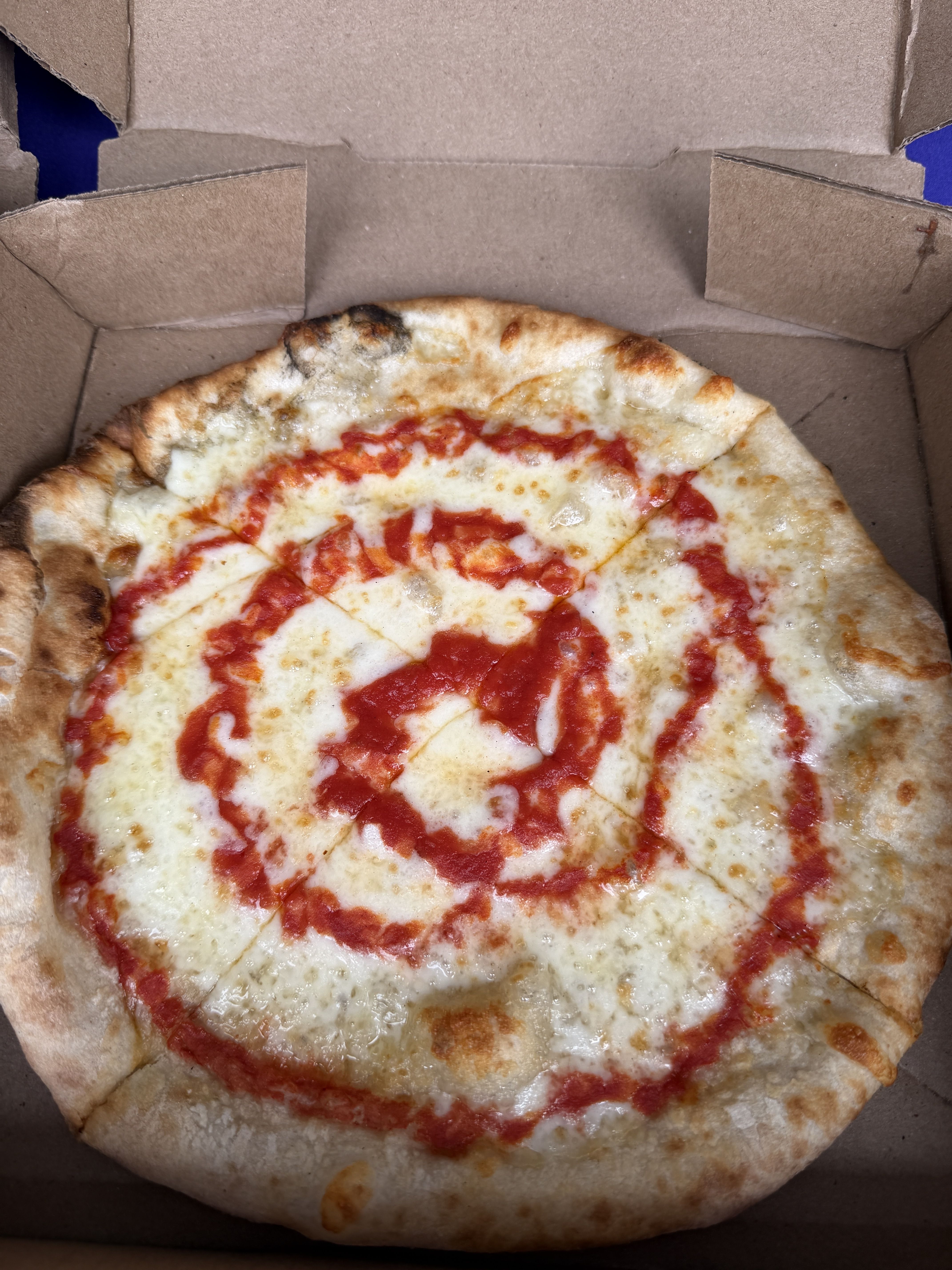 Round cheese pizza with melted mozzarella and bright red tomato sauce, in an open cardboard pizza box; golden-brown crust.