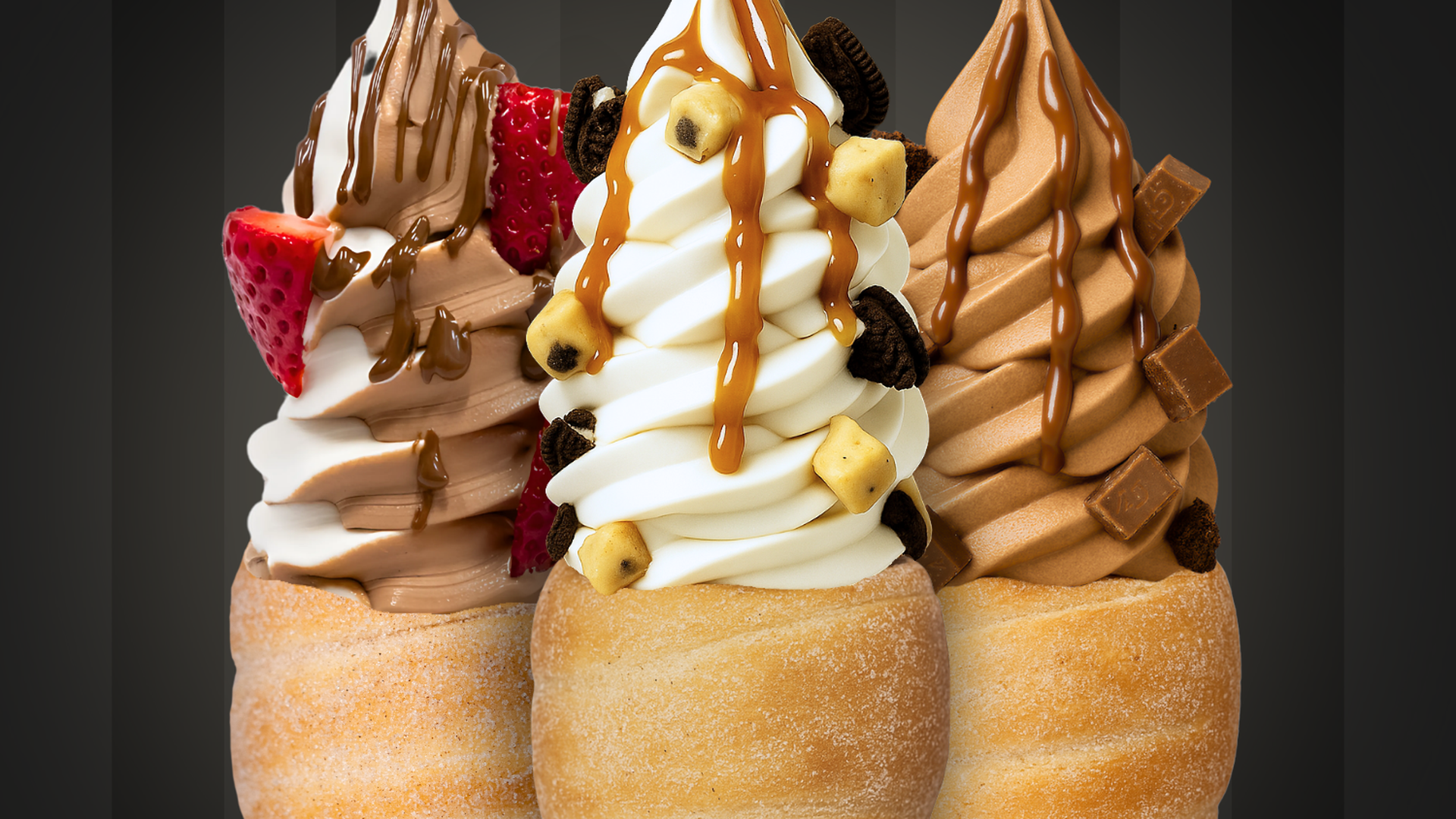 Four ice cream cones with chocolate and vanilla swirls, topped with caramel, cookies, brownie bits, a strawberry slice, and chocolate squares against a dark striped background.
