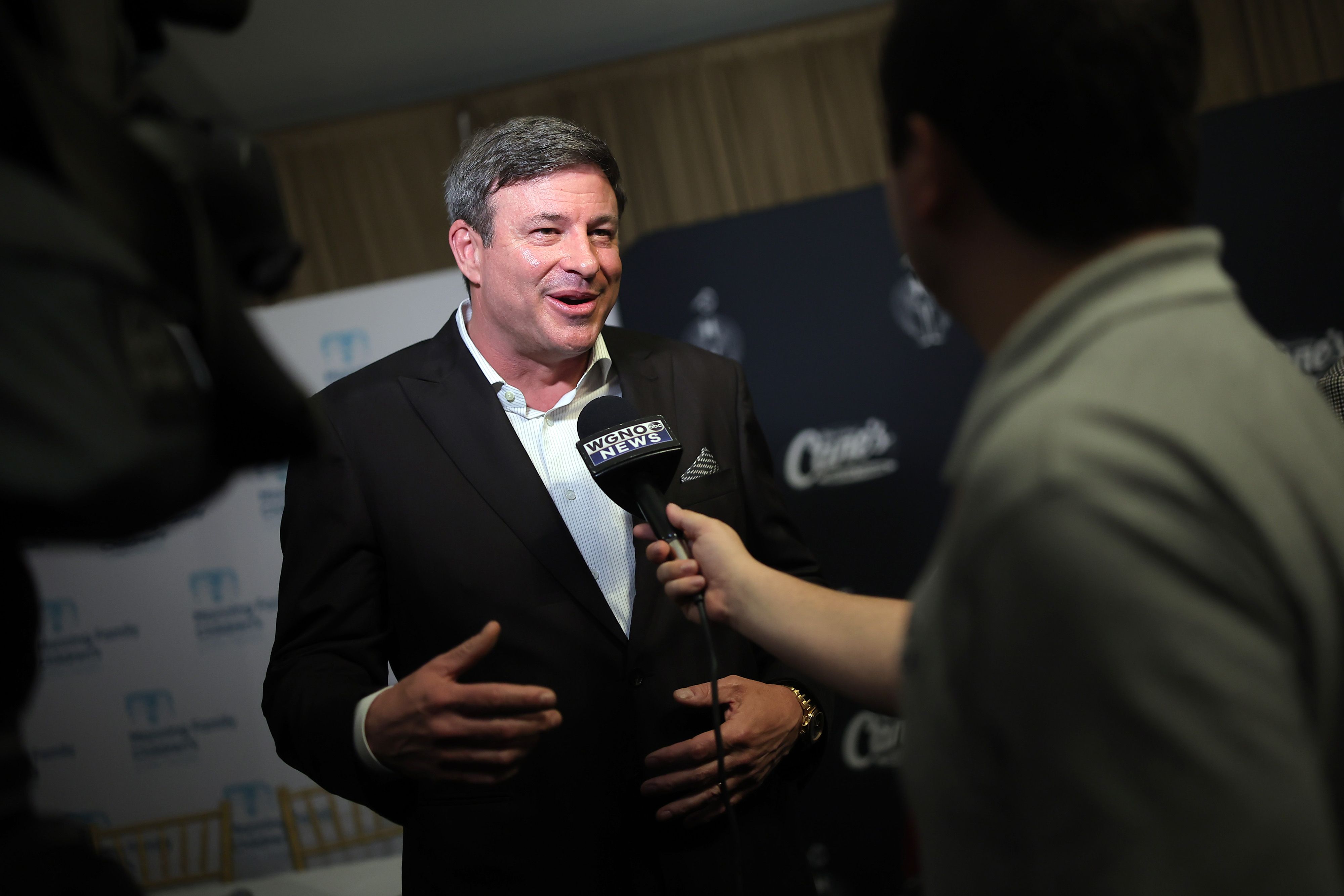Todd Graves wears a suit and talks into a microphone being held by a male reporter.