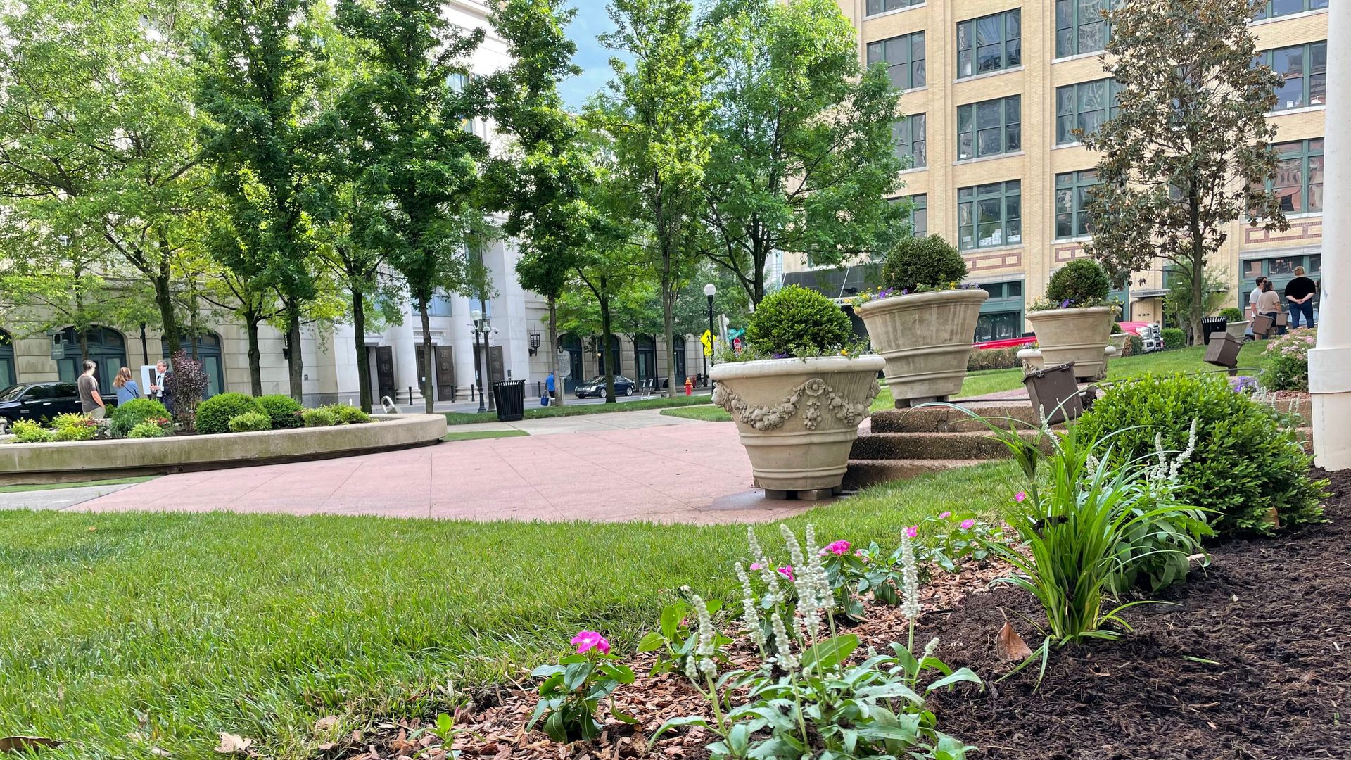 A lush grassy plaza with a fountain in the middle and people gathered around a center courtyard.