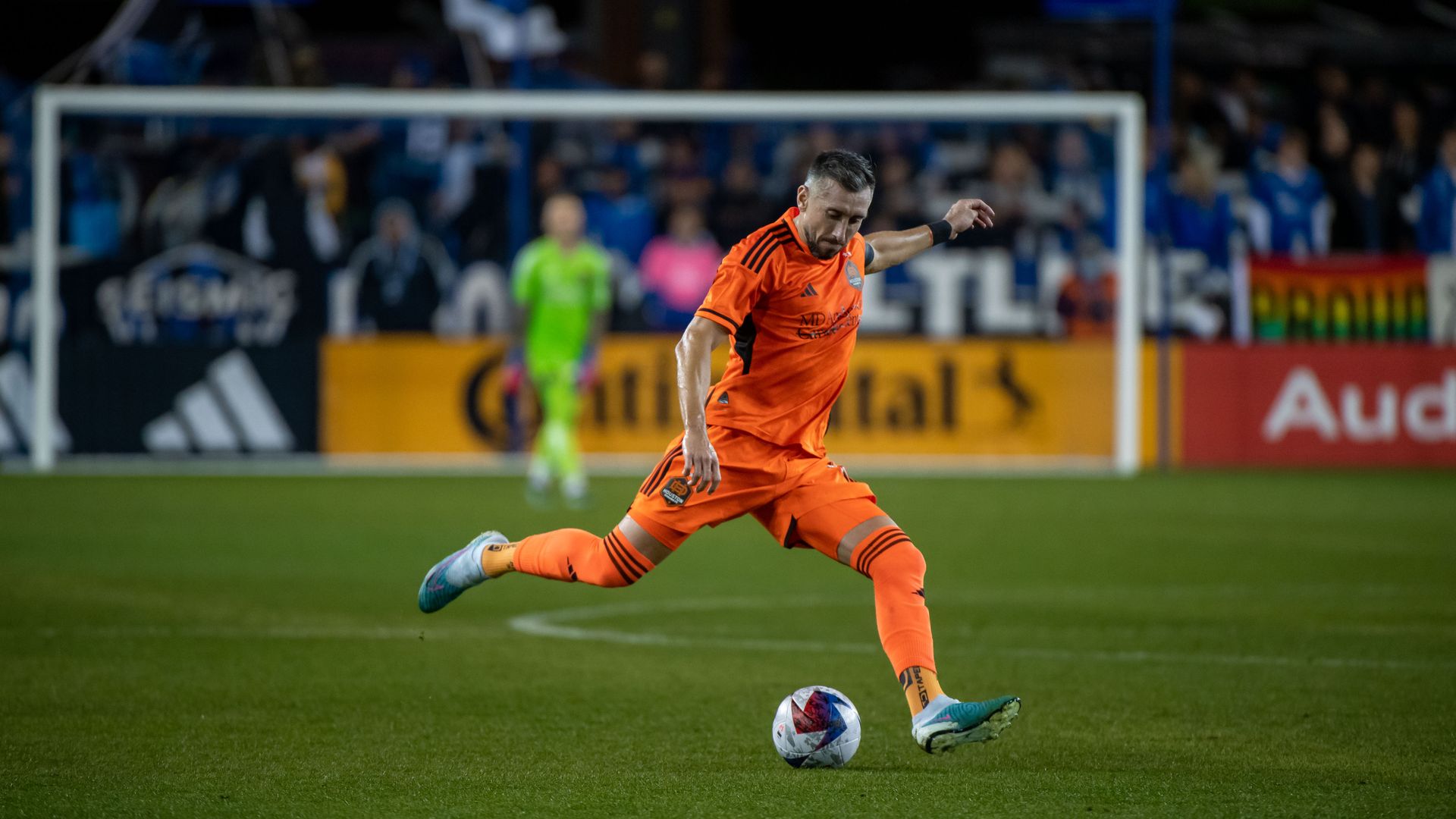 The Dynamo's Hector Herrera, wearing an orange professional soccer uniform, sets up a kick 